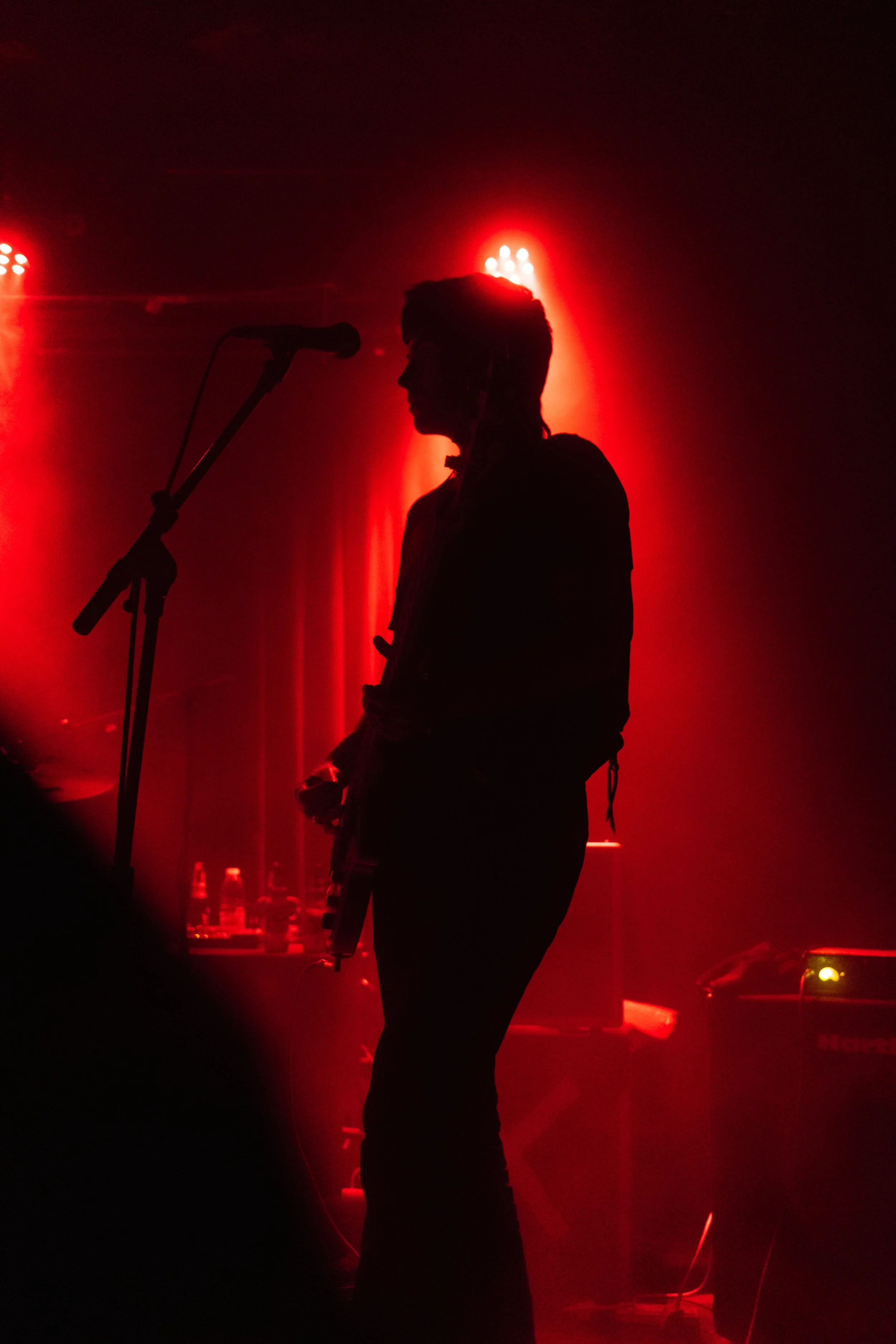 Silhouette of a musician standing next to a microphone on stage with dramatic red lighting.