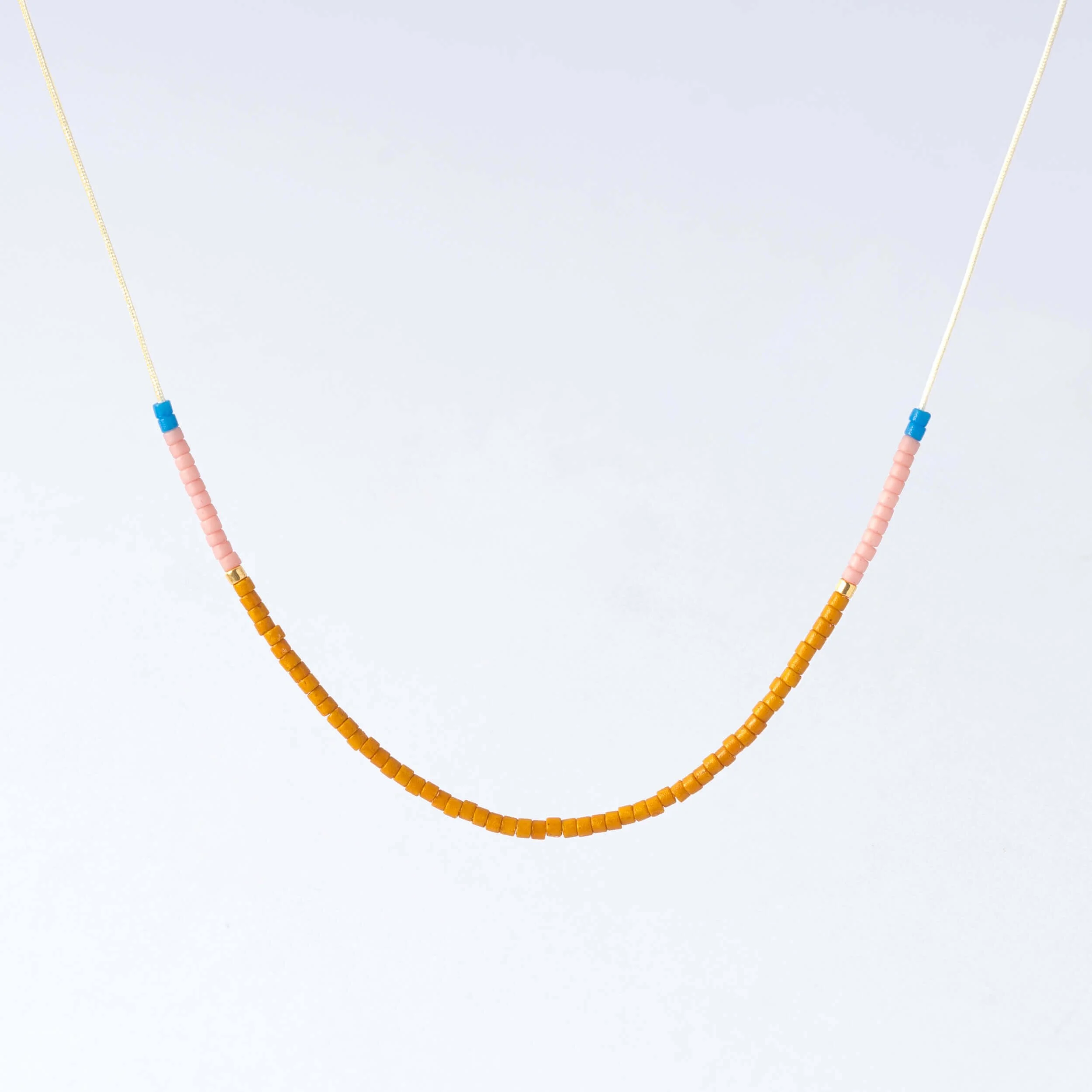 Filigrane Halskette aus kleinen Glasperlen in Honig, Rosa und Himmelblau auf cremefarbenem Nylonfaden mit goldfarbenen Details