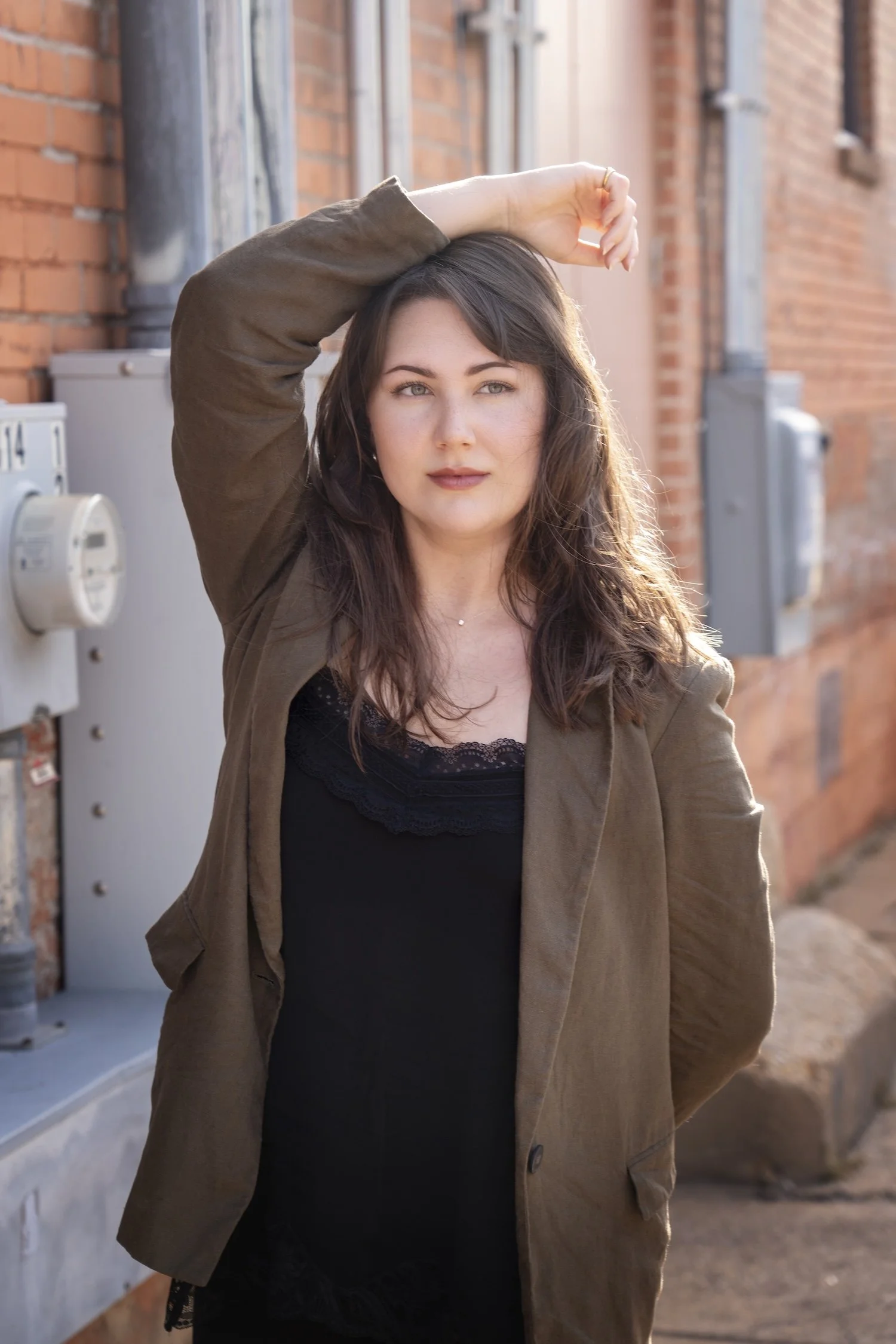 Megan, writer at Bigmouth Copy, wears a black blouse and brown blazer. She looks off to the side with a gentle smile, her right arm draped over the top of her head.