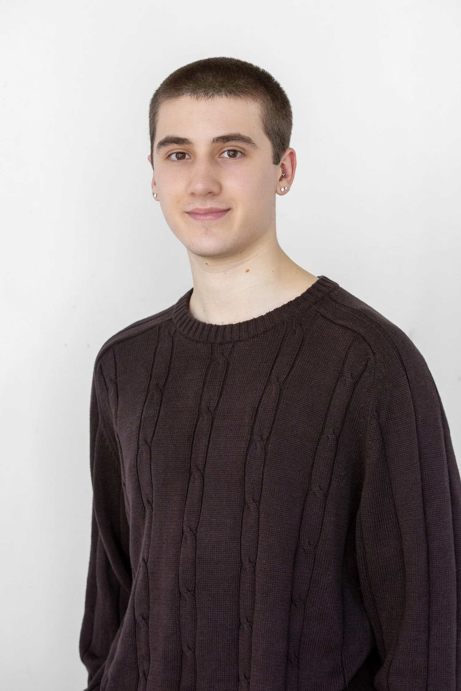 An indoor headshot of Dax. He wears a black long sleeved tee and is smiling softly at the camera.