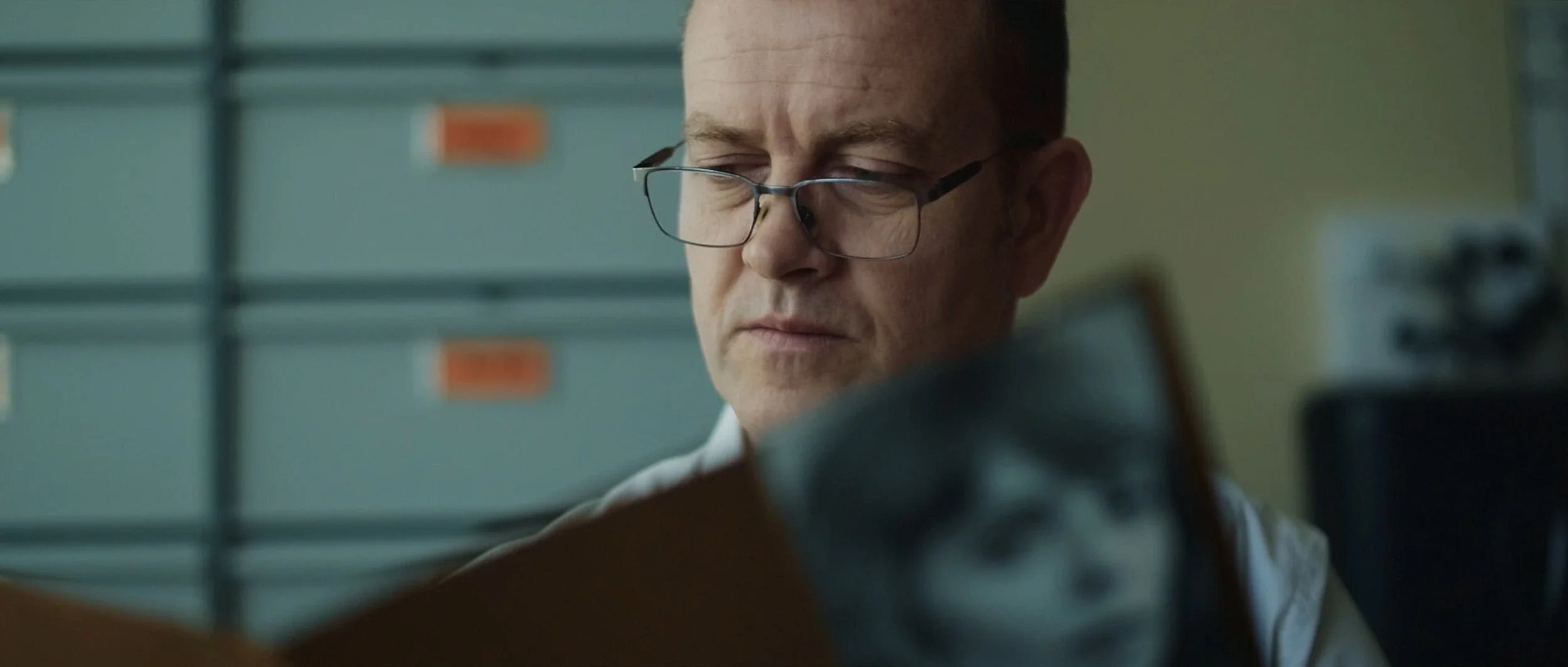 the-hire-short-film-man-glasses-examining-document.webp