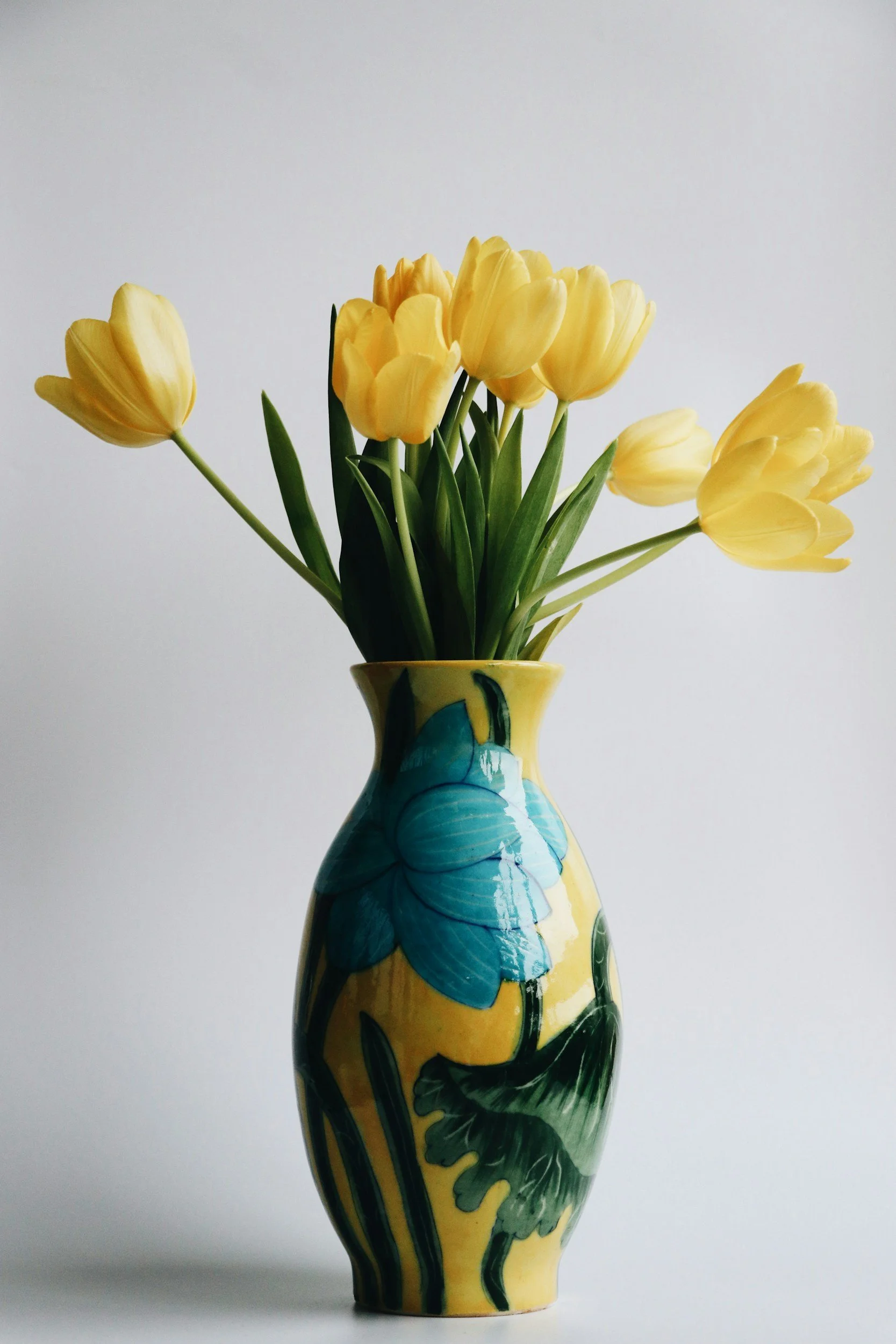 A yellow, blue and green decorative vase with yellow tulip flowers in it