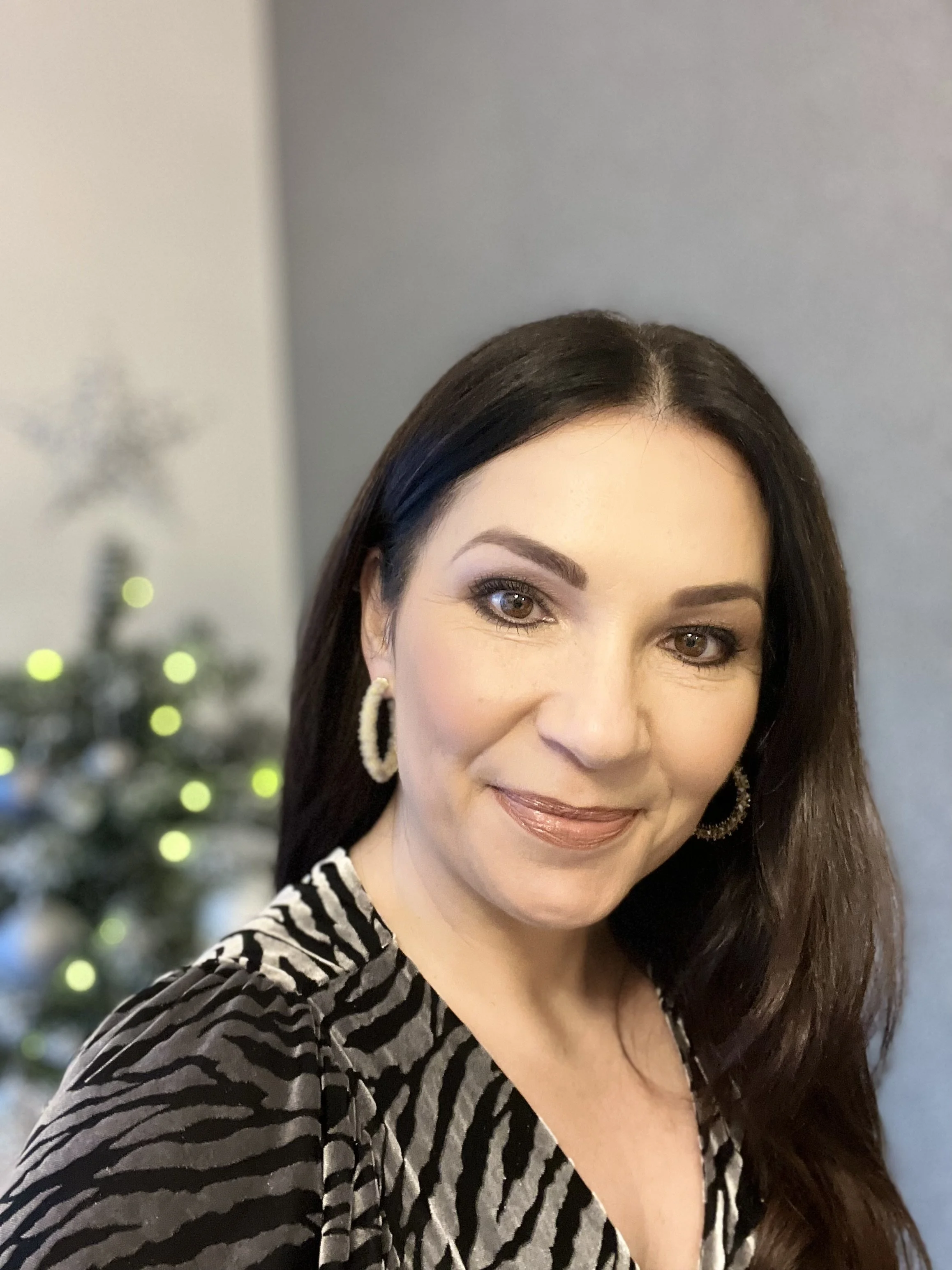 Nicola Farndell with dark brown hair smiling in front of a Christmas tree with silver decorations as she explores how to support your health at Christmas.