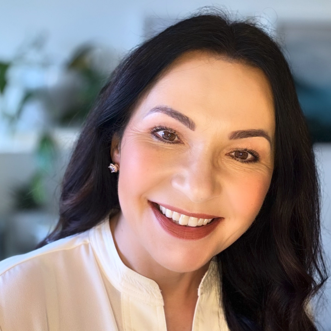 A woman with dark brown hair and brown eyes smiling, wearing a cream blouse and gold earrings as she shares insights to live healthy and strong through menopause. the