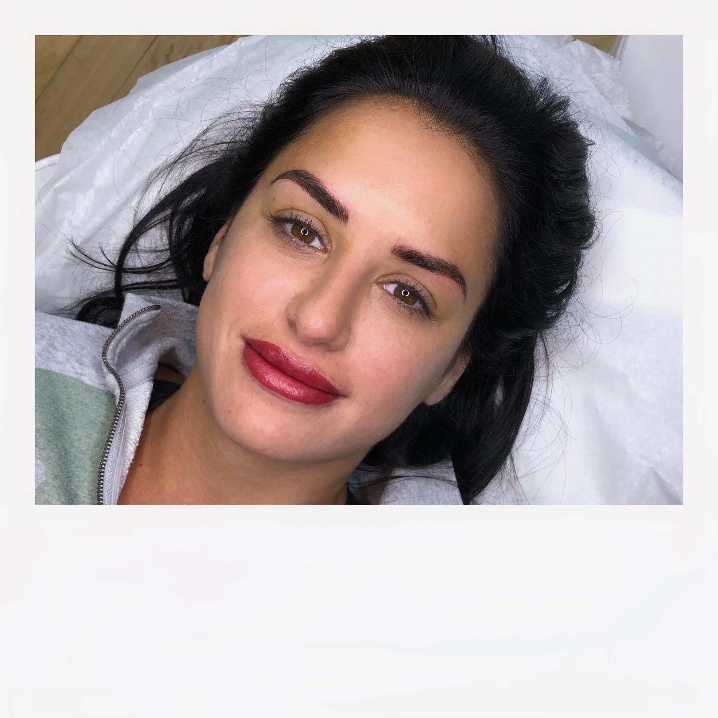 Close-up of a woman with dark hair, light skin, brown eyes, wearing lipstick, lying down on a white pillow.