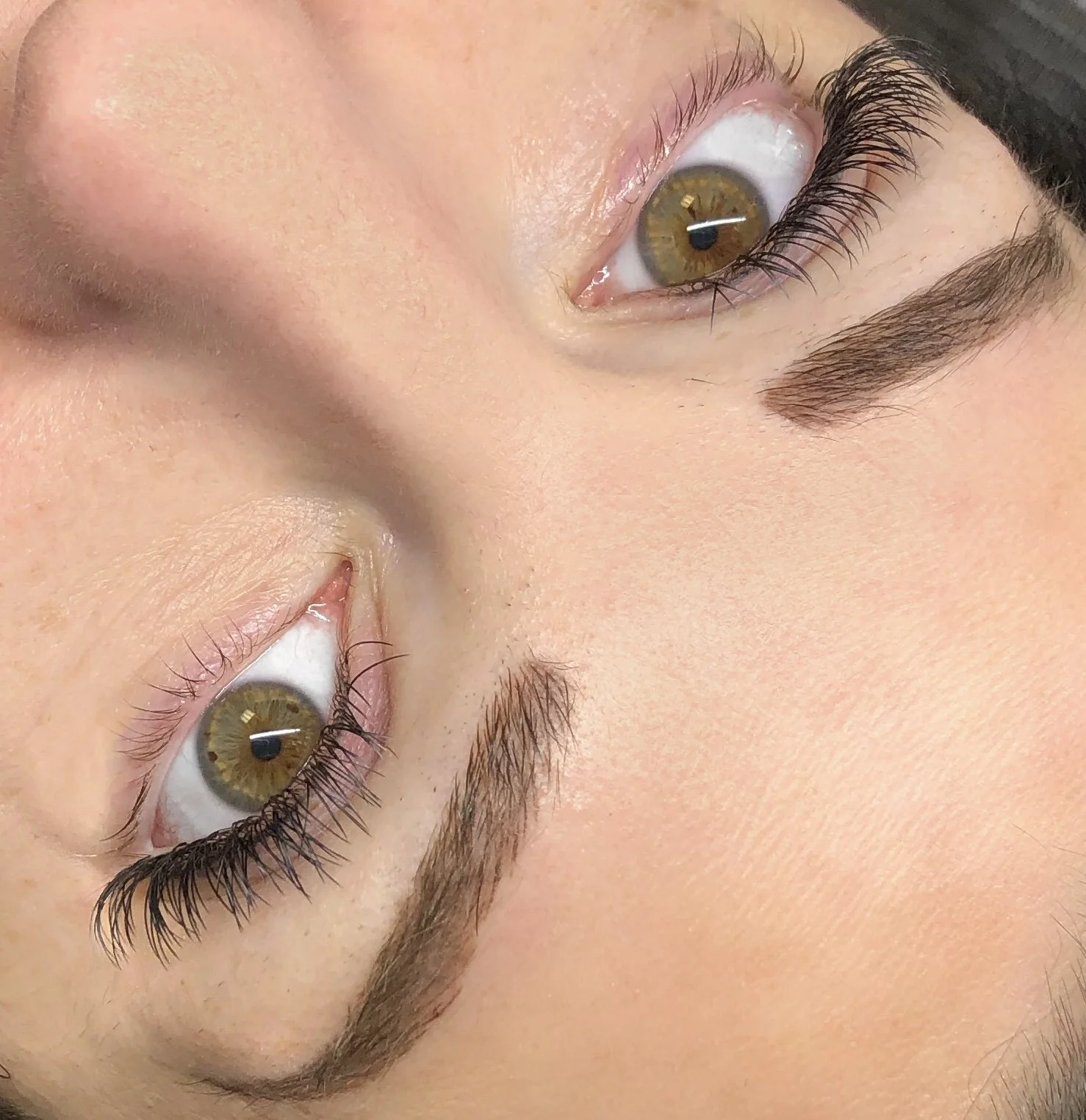 Close-up of a person's face, showing hazel eyes, extended eyelashes, and well-groomed eyebrows, with skin appearing smooth and clear.