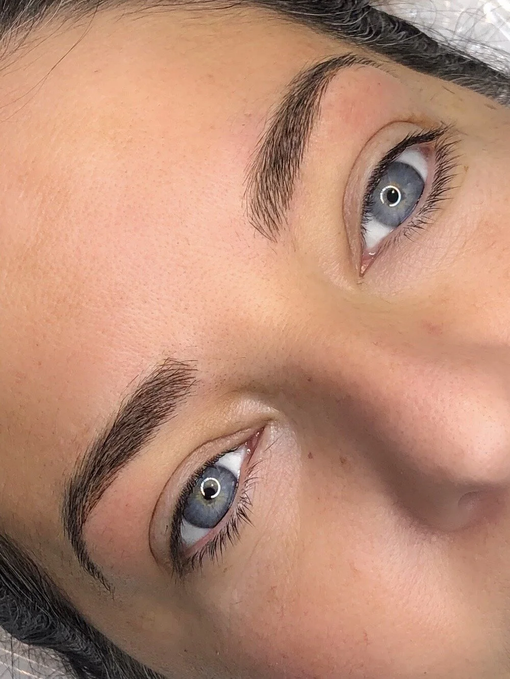 Close-up of a woman's face with blue eyes, well-groomed eyebrows, and smooth skin.