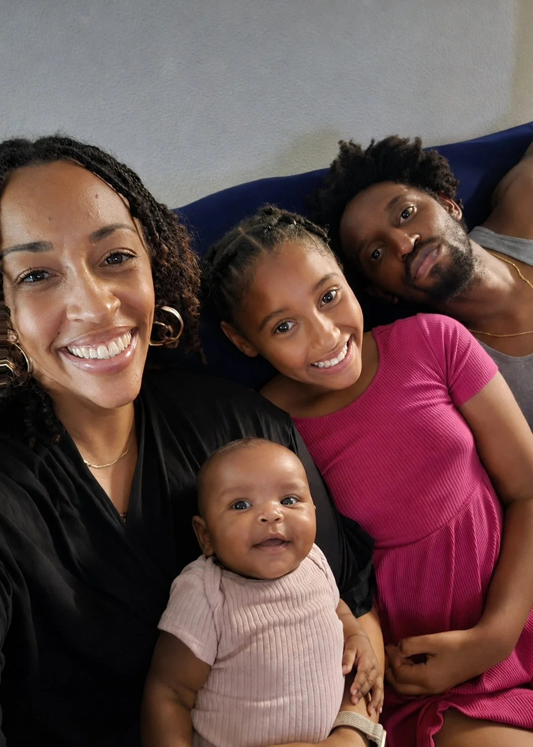 African American family picture sitting on a sofa togeher with the mother holding infant girl, pre-adolescent big sister, and father sitting together
