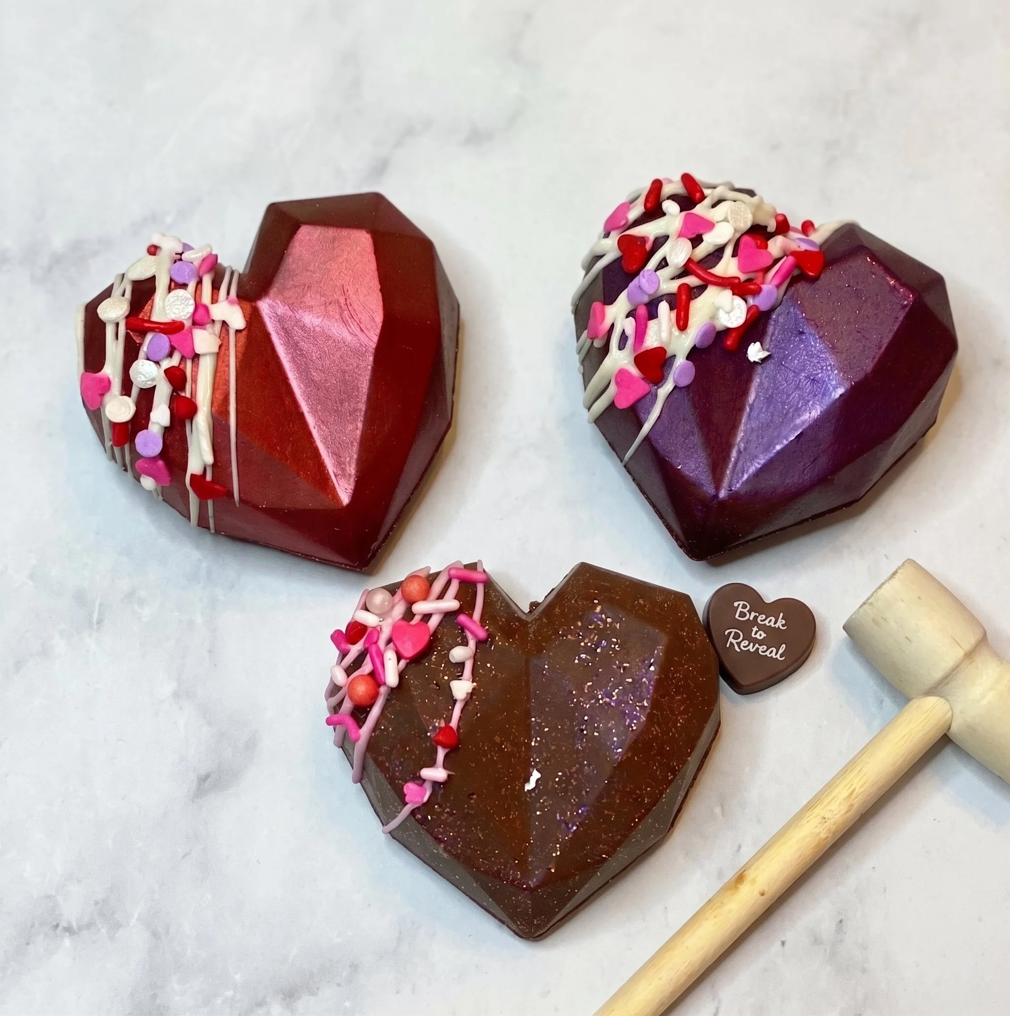 Assorted geometric heart chocolate bombs with a mini smash hammer