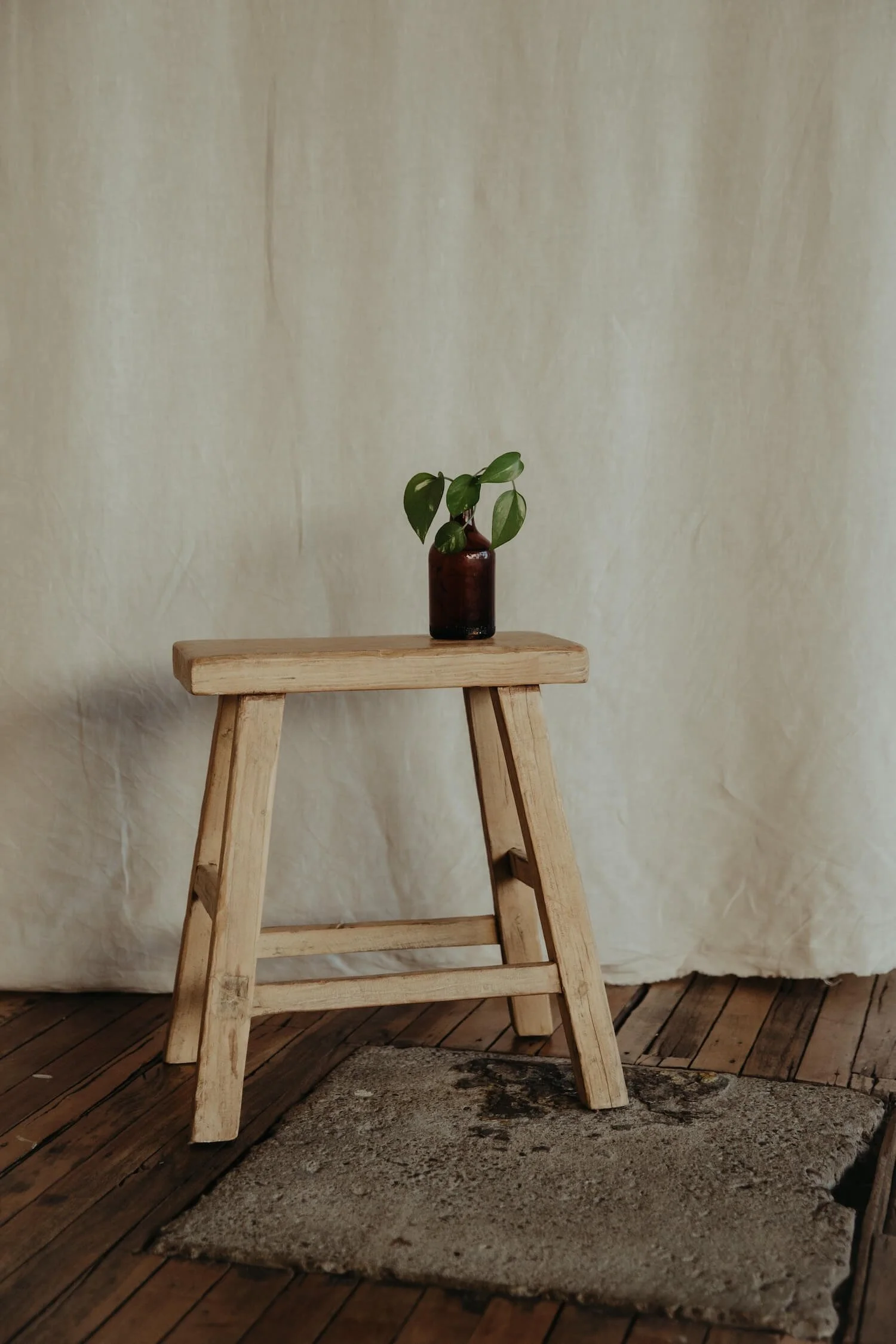 Brown glass vase with plant clipping on a timber stool