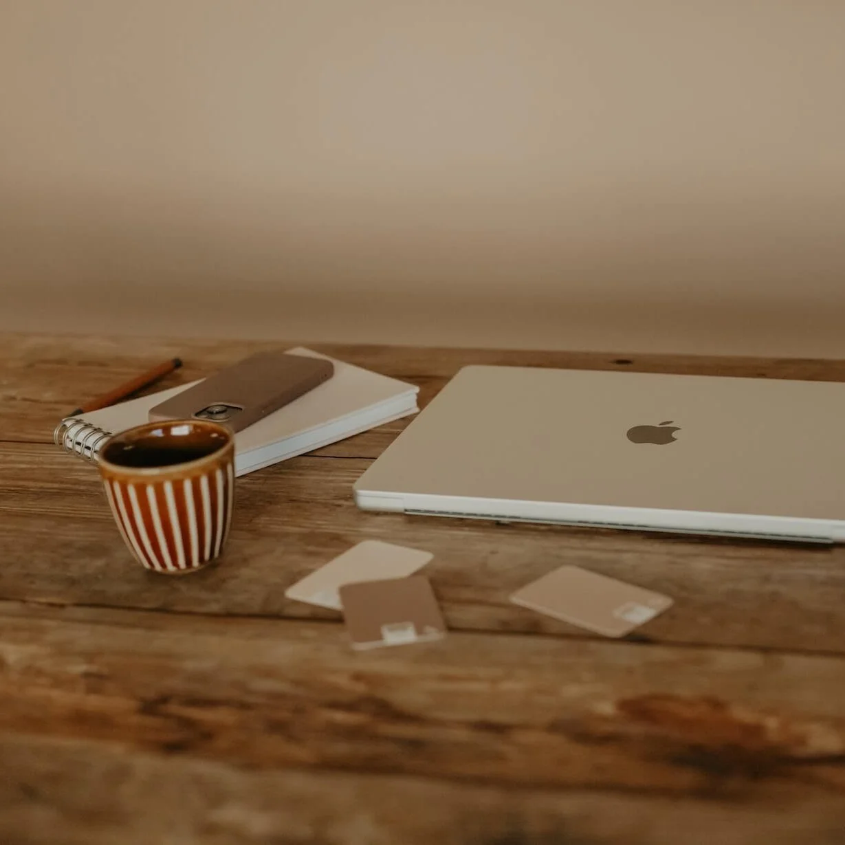 A simple wooden desk with a closed laptop, notebook, pencil and a cup of coffee, styled to reflect a calm, focused approach to online visibility and planning.