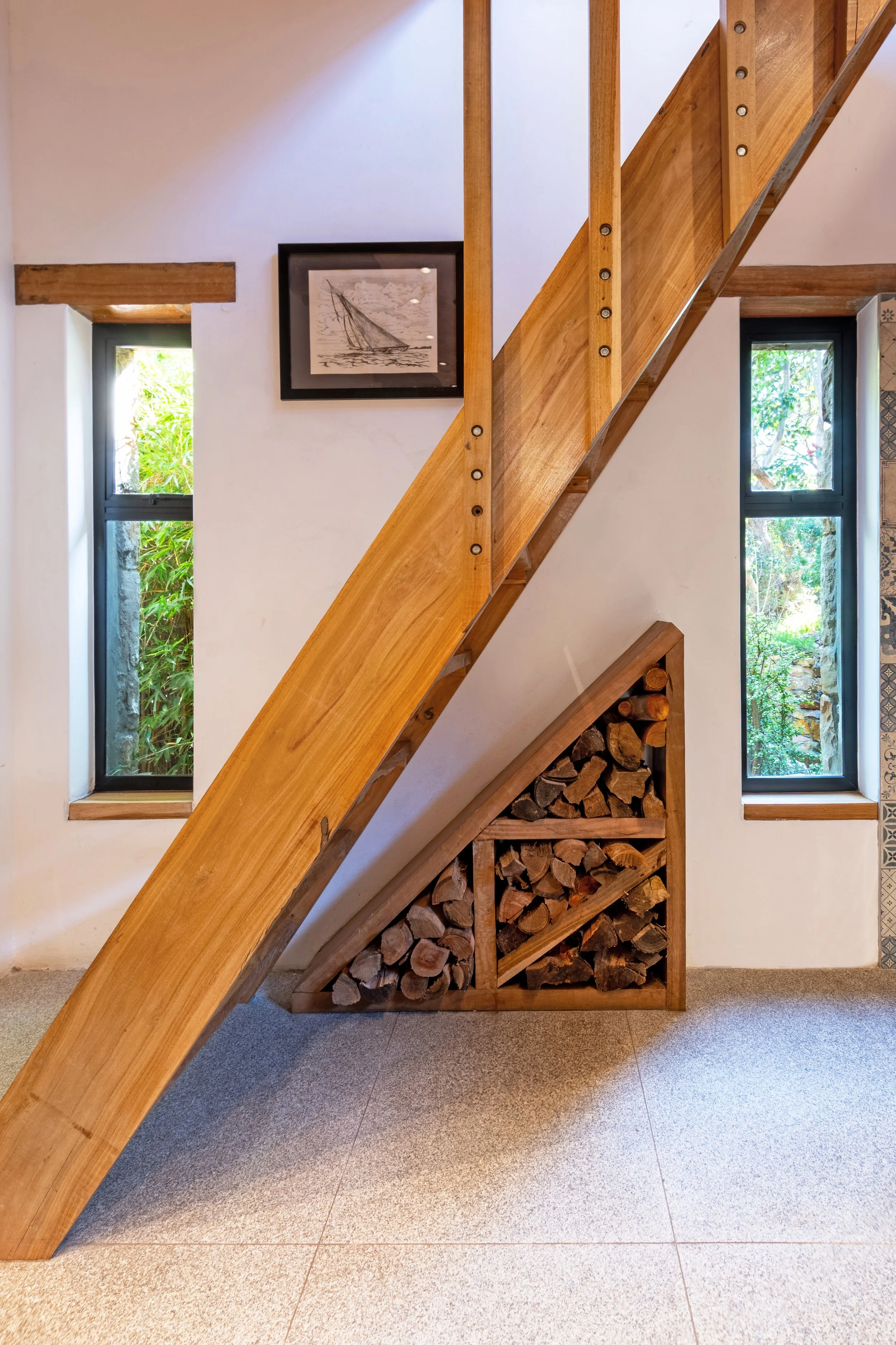 Interior wall with windows, a wooden staircase, and a firewood storage area.