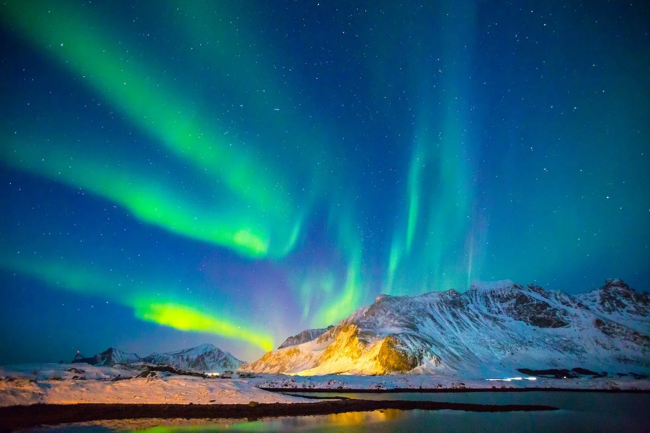 Northern Lights over snow-covered mountains and water, starry sky.