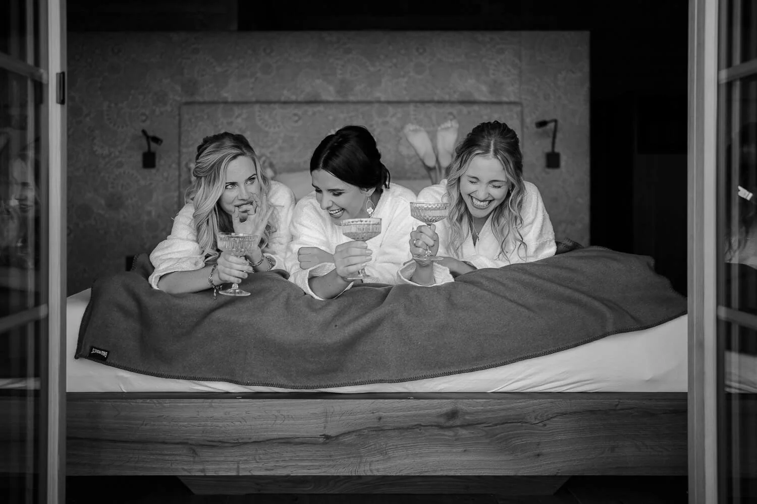 Braut mit Freundinnen im Bademantel, lachend mit Sektgläsern