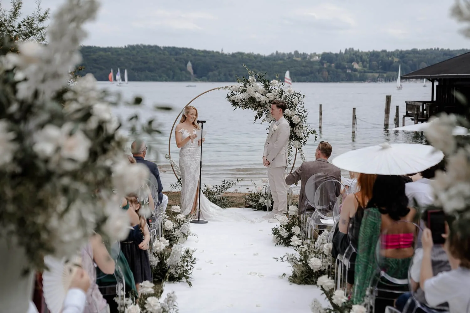 Hochzeit Floristik am See: Brautpaar vor Blumenbogen und weißem Teppich