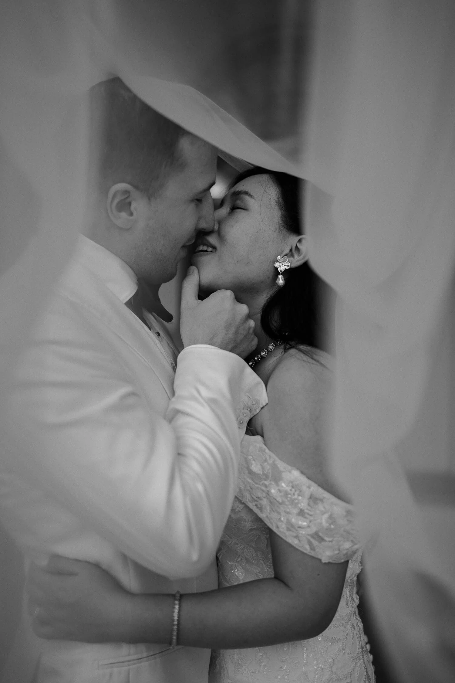 Emotionales Hochzeitsfoto in München – Braut und Bräutigam küssen sich verliebt unter dem Schleier.