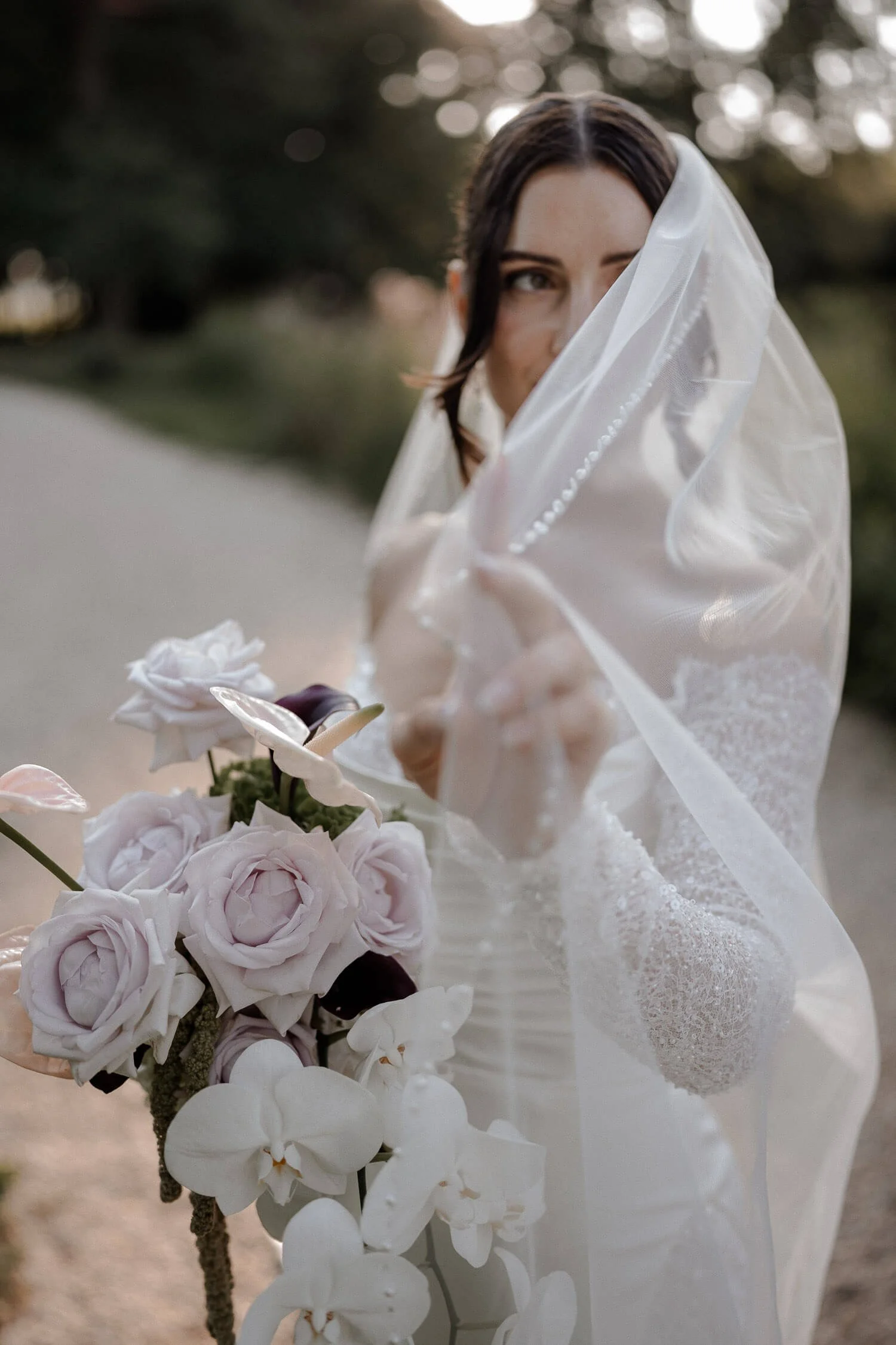 Romantische Braut in Schloss Hohenkammer bei München hält ihren Schleier vor das Gesicht, mit elegantem Brautstrauß
