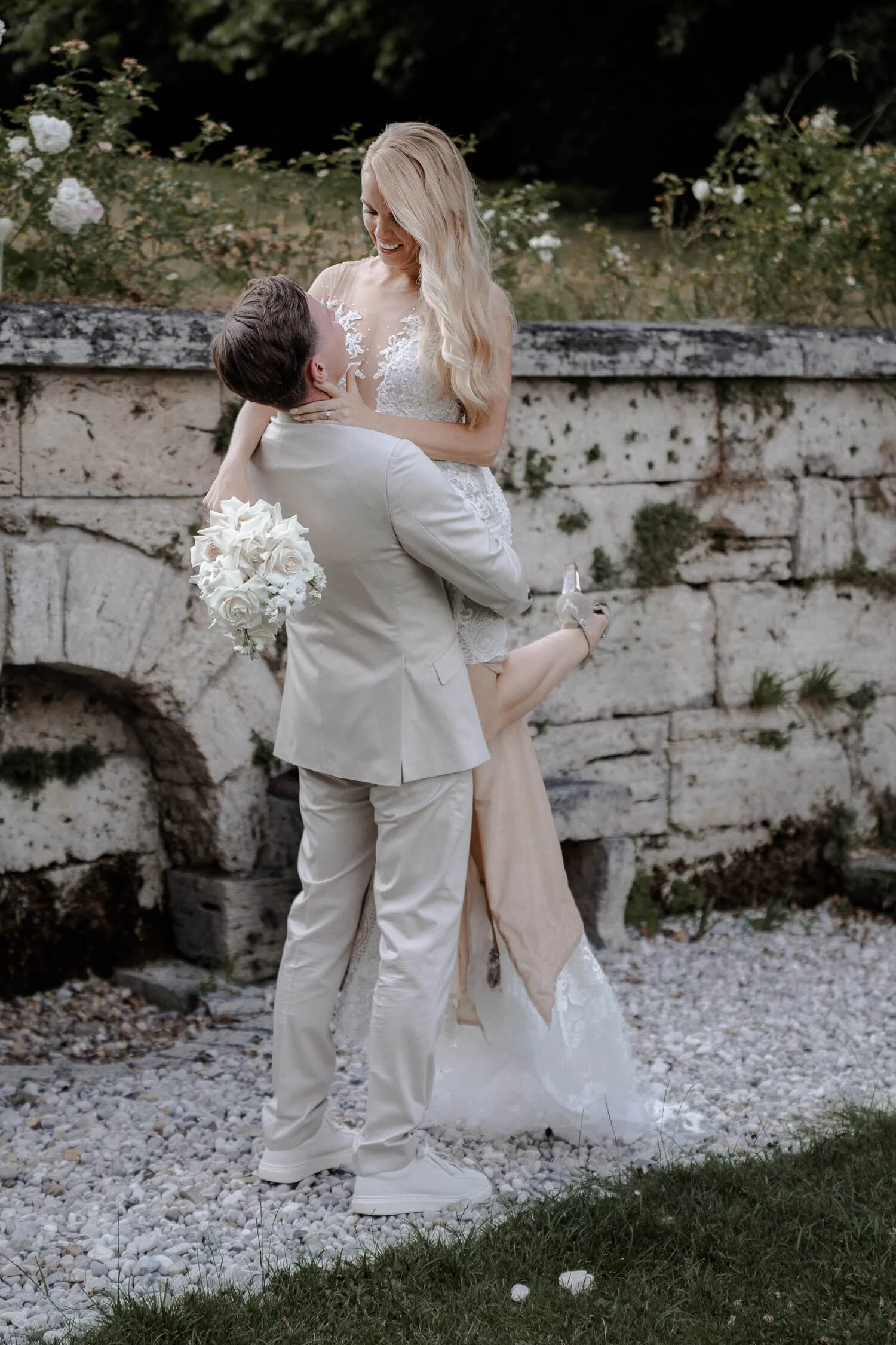 Bräutigam hebt Braut lachend hoch vor Natursteinwand beim La Villa am Starnberger See