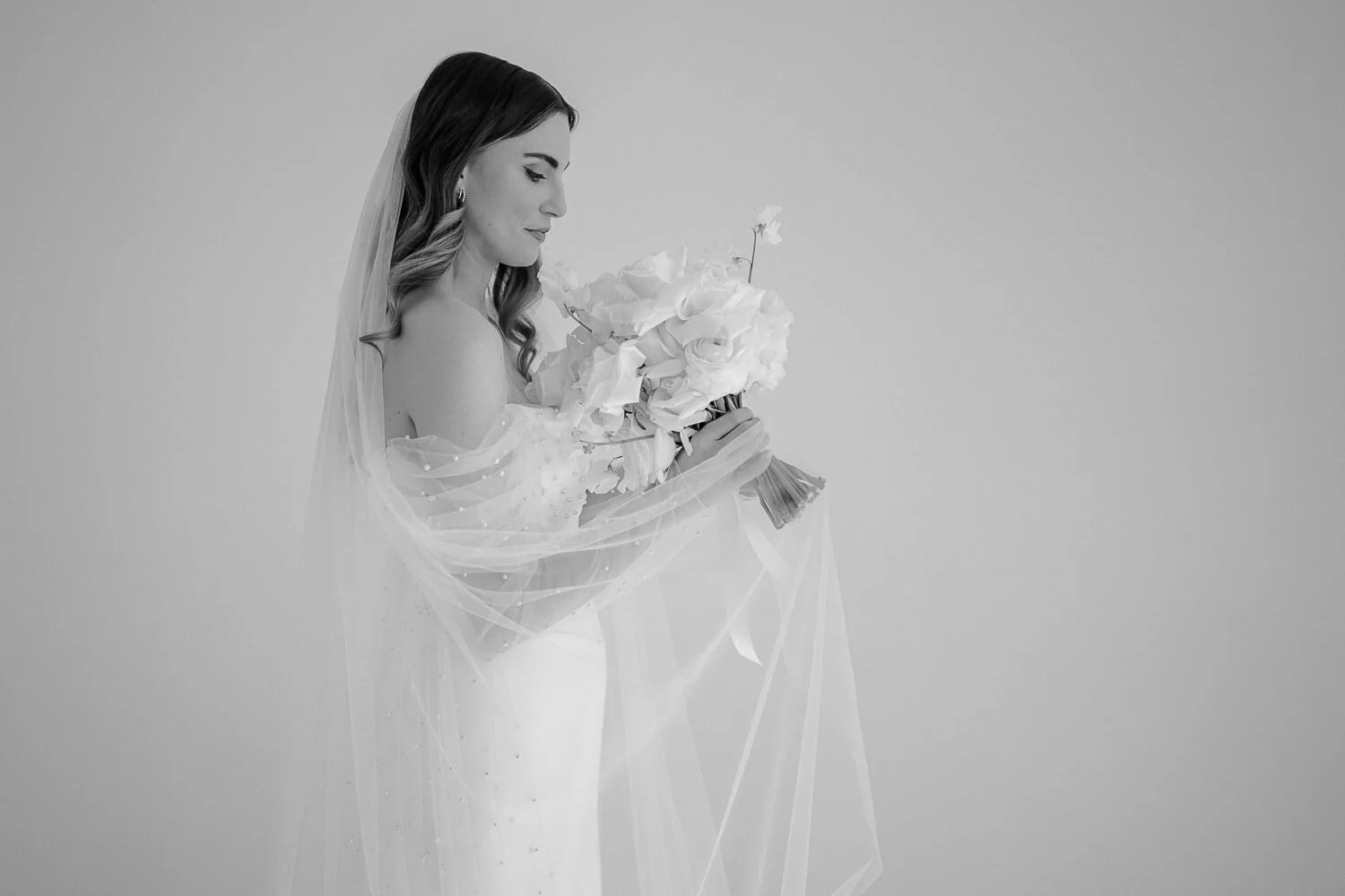 Braut mit Schleier und Strauß vor hellem Hintergrund