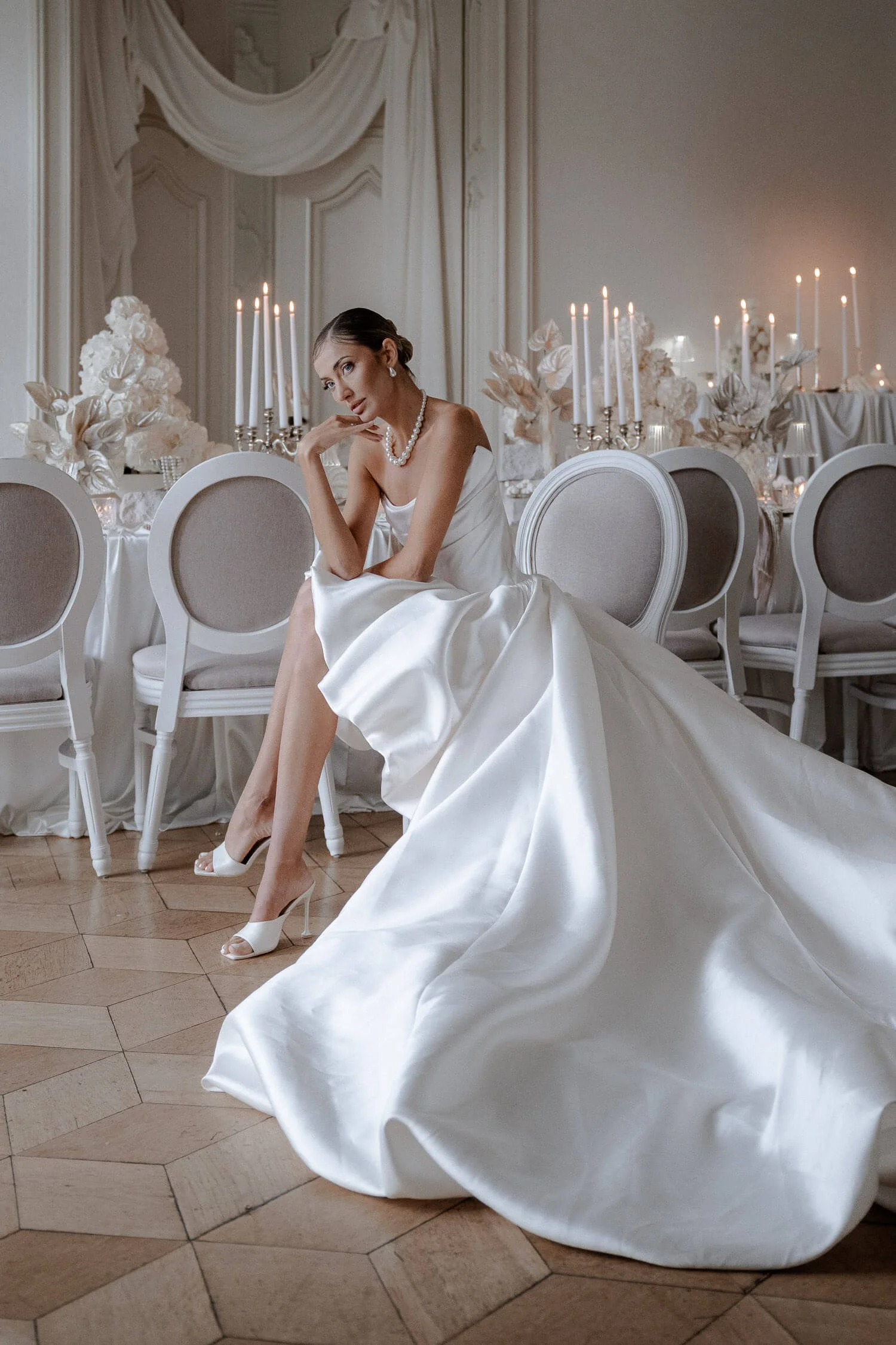 Brautkleid München: Braut sitzt im eleganten Satin-Brautkleid im festlichen Saal mit Kerzen