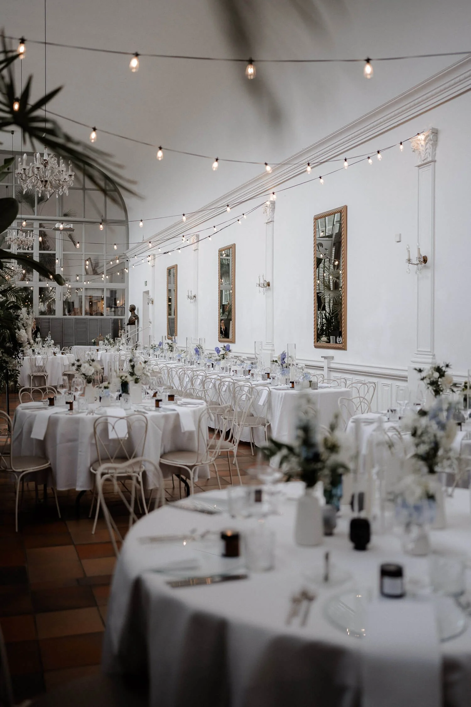 Stilvolle Hochzeitslocation – das Schlosscafè Palmenhaus in München mit weißer Dekoration und Lichterketten
