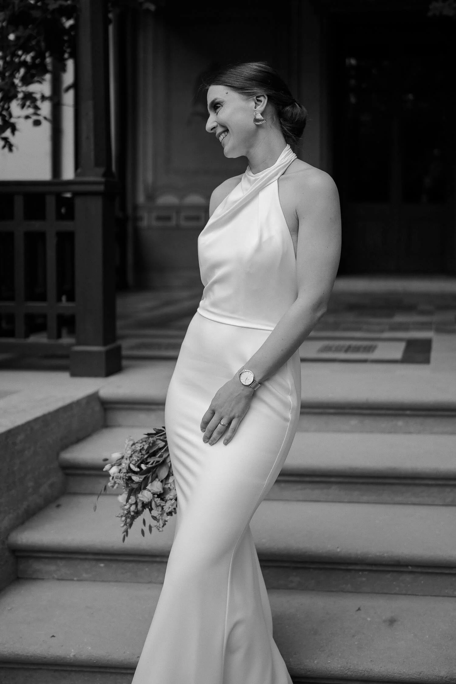 Schwarzweiß: Braut allein auf Treppe vor Eingang (Bouquet, candid smile) – braut solo roseninsel treppe