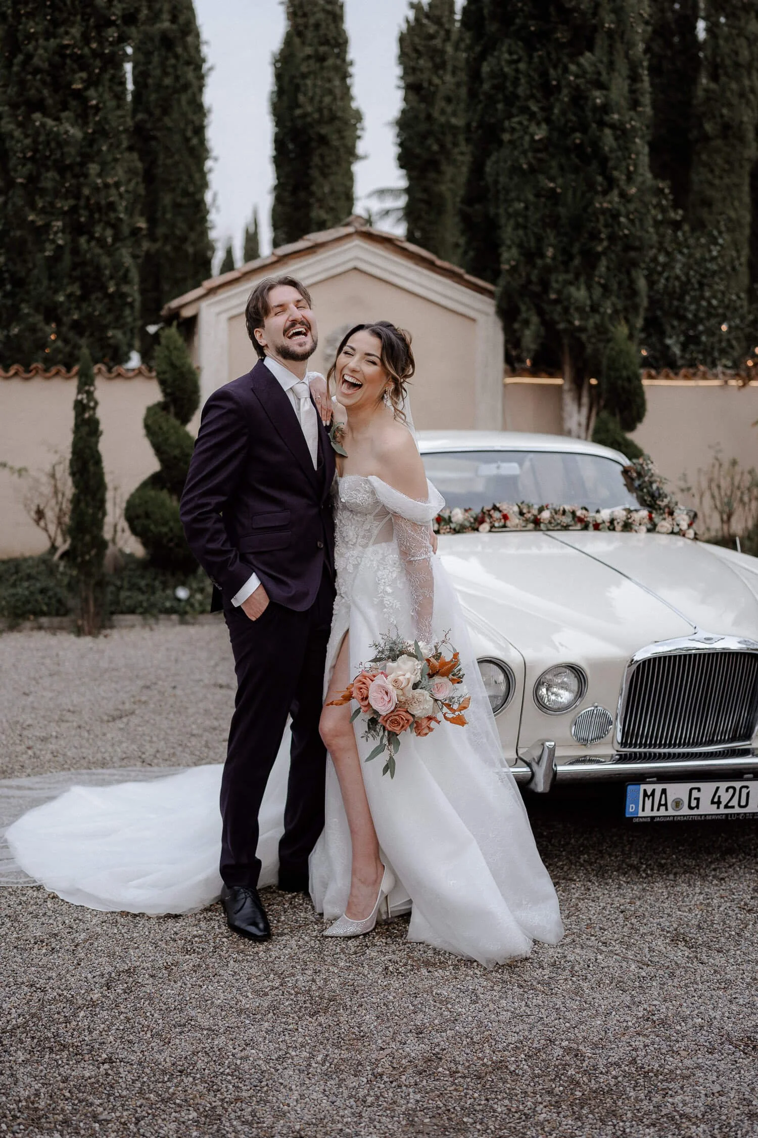 Lachendes Brautpaar vor Oldtimer im Morrhof – Hochzeitsfotograf Sara Wolff