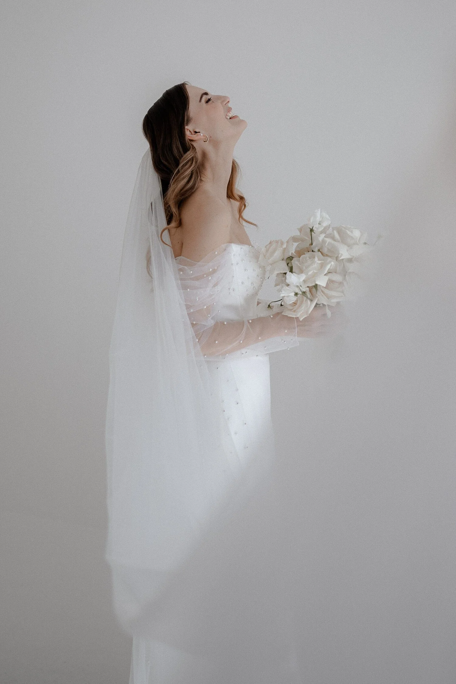 Eine Braut lacht nach dem Getting Ready vor einer schlichten weißen Wand.