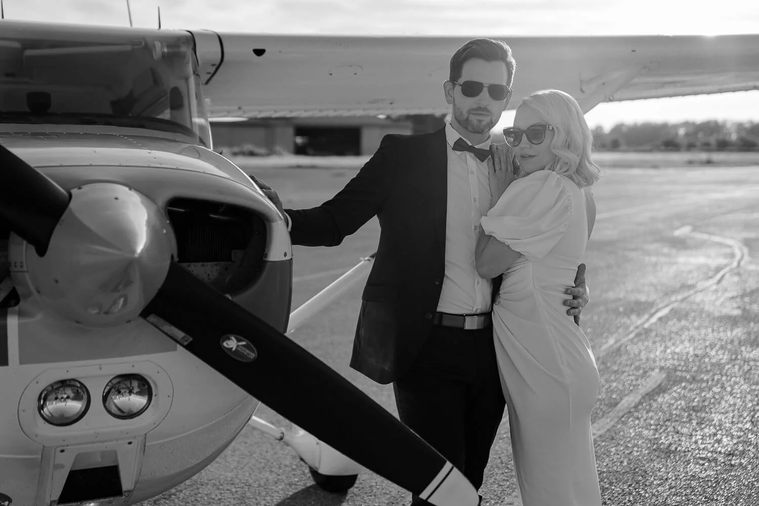 Couple posing next to small airplane at golden hour