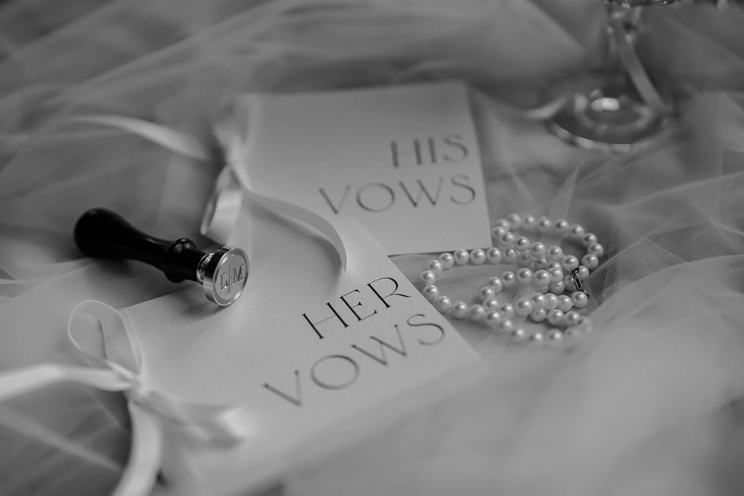 Stilvolle Hochzeitsdetails – Eheversprechen mit Perlenkette und Siegel auf feinem Schleier.