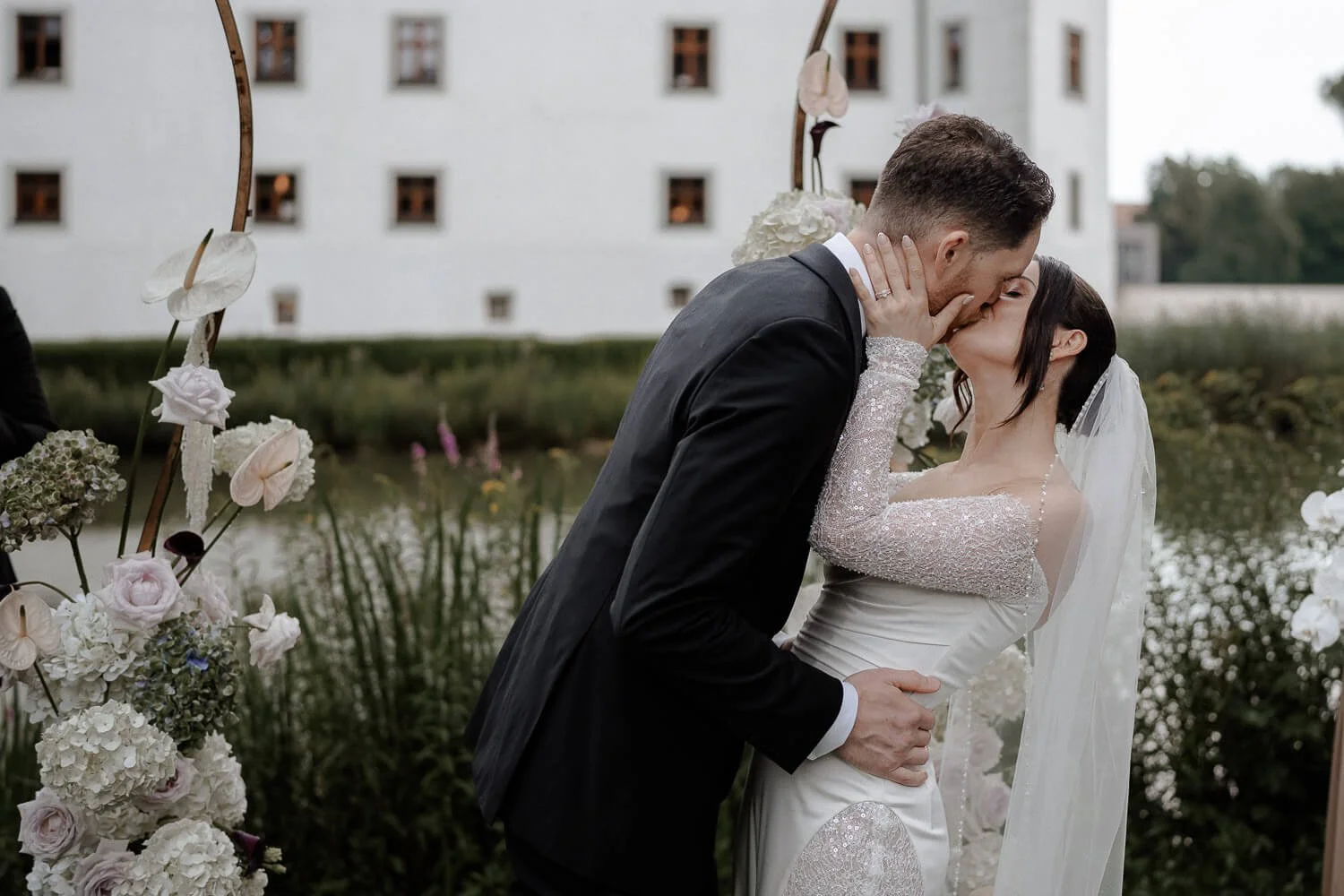 Elegantes Brautpaar küssend unter dem Traubogen von Schloss Hohenkammer bei der Hochzeit