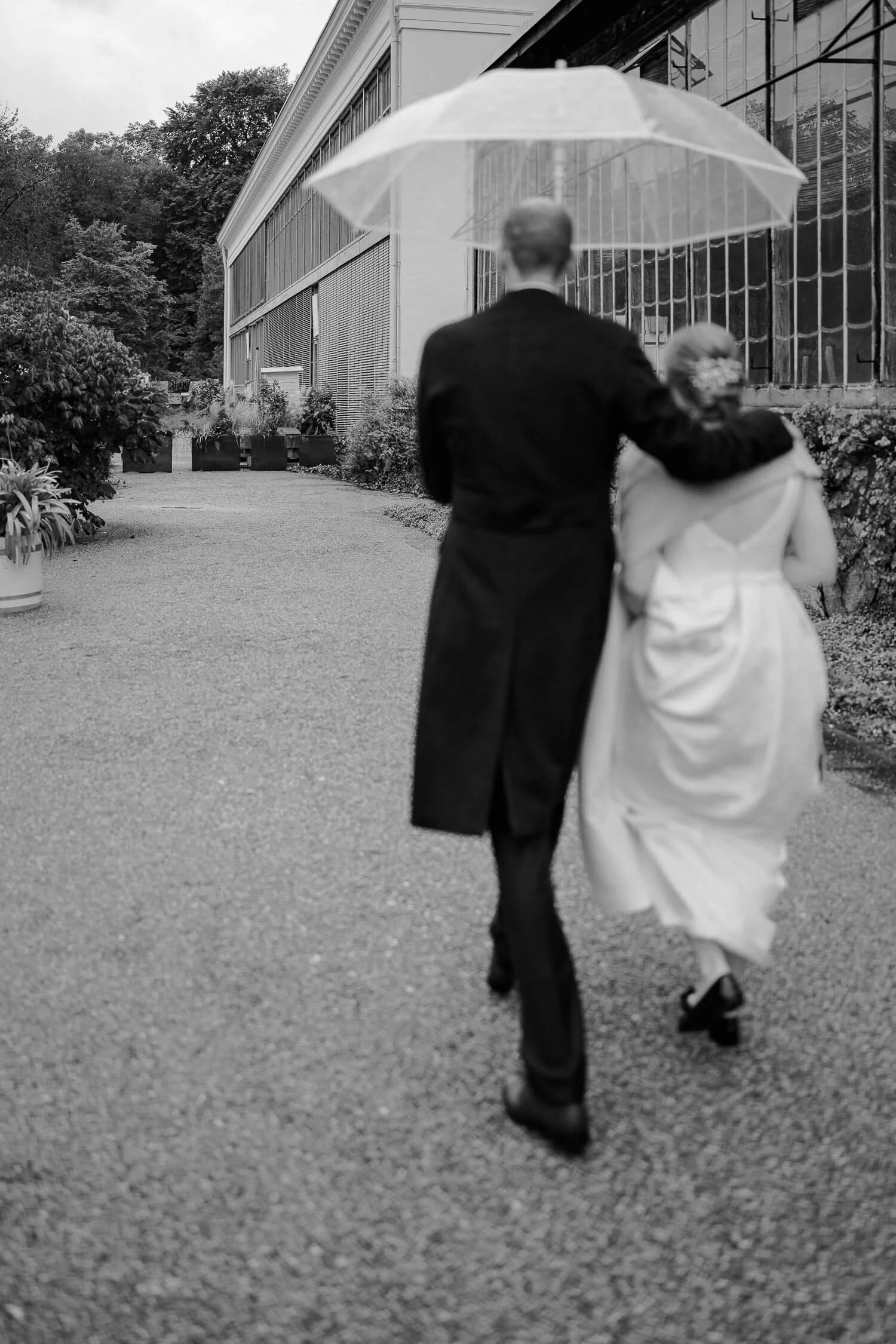 Brautpaar mit Schirm auf Weg zur Hochzeit im Palmenhaus München