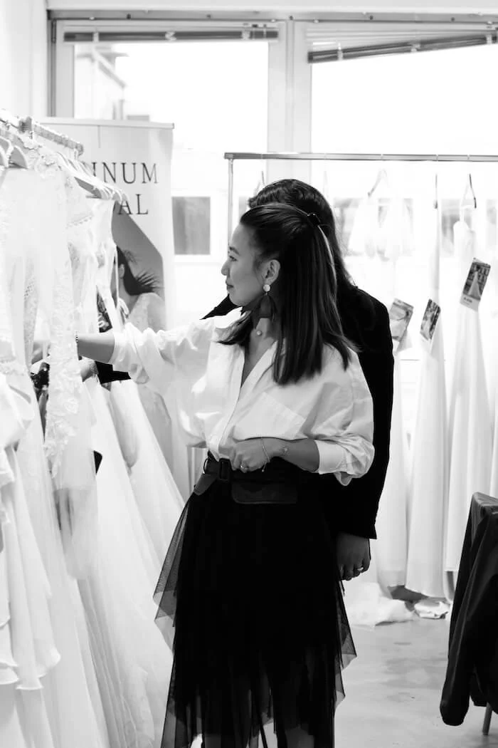 Brautkleid München: Beratung im Store, Kundin betrachtet Spitzenkleider am Ständer