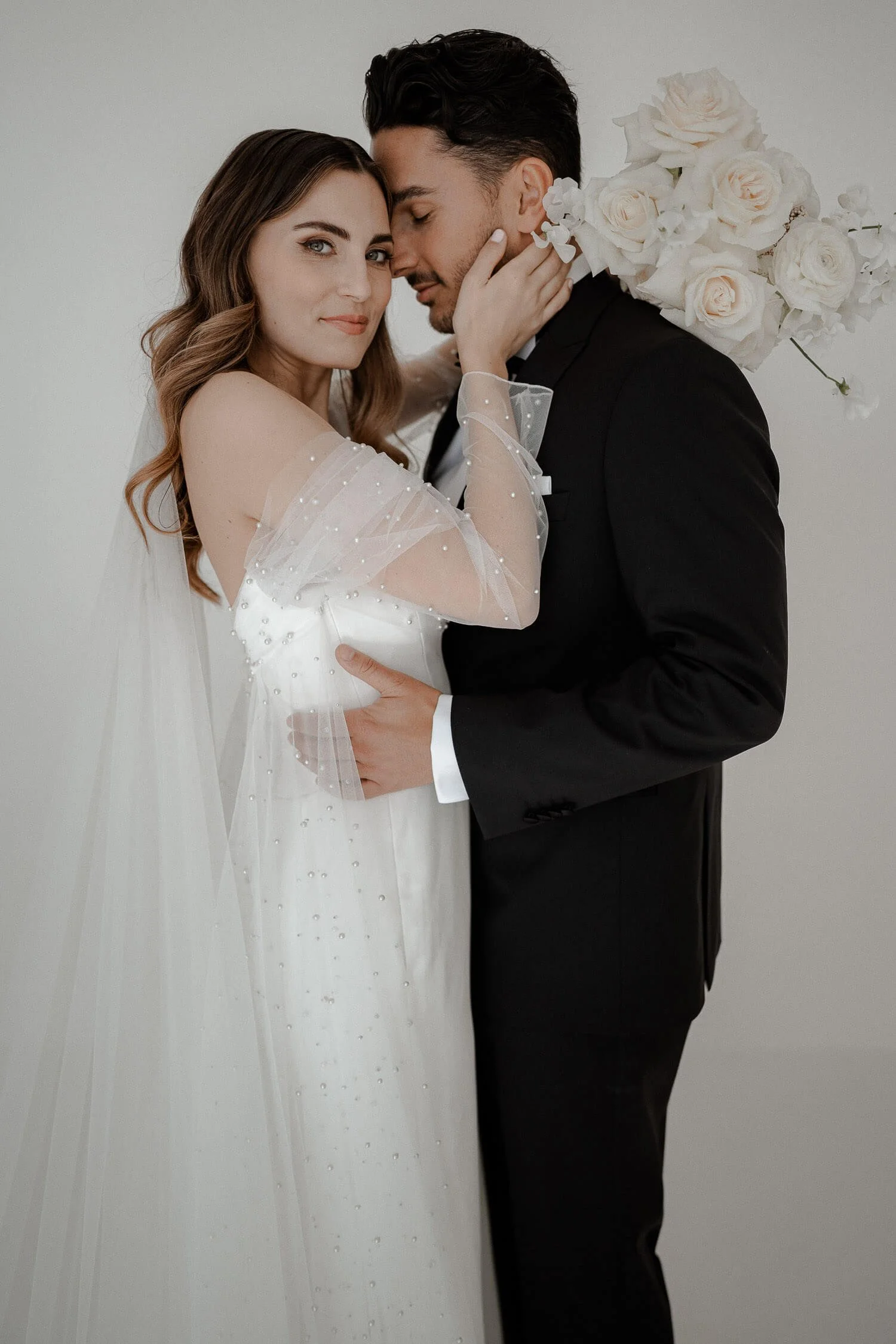 Elegantes Brautpaar innig umarmt vor weißem Hintergrund, fotografiert von einem Hochzeitsfotografen in München.