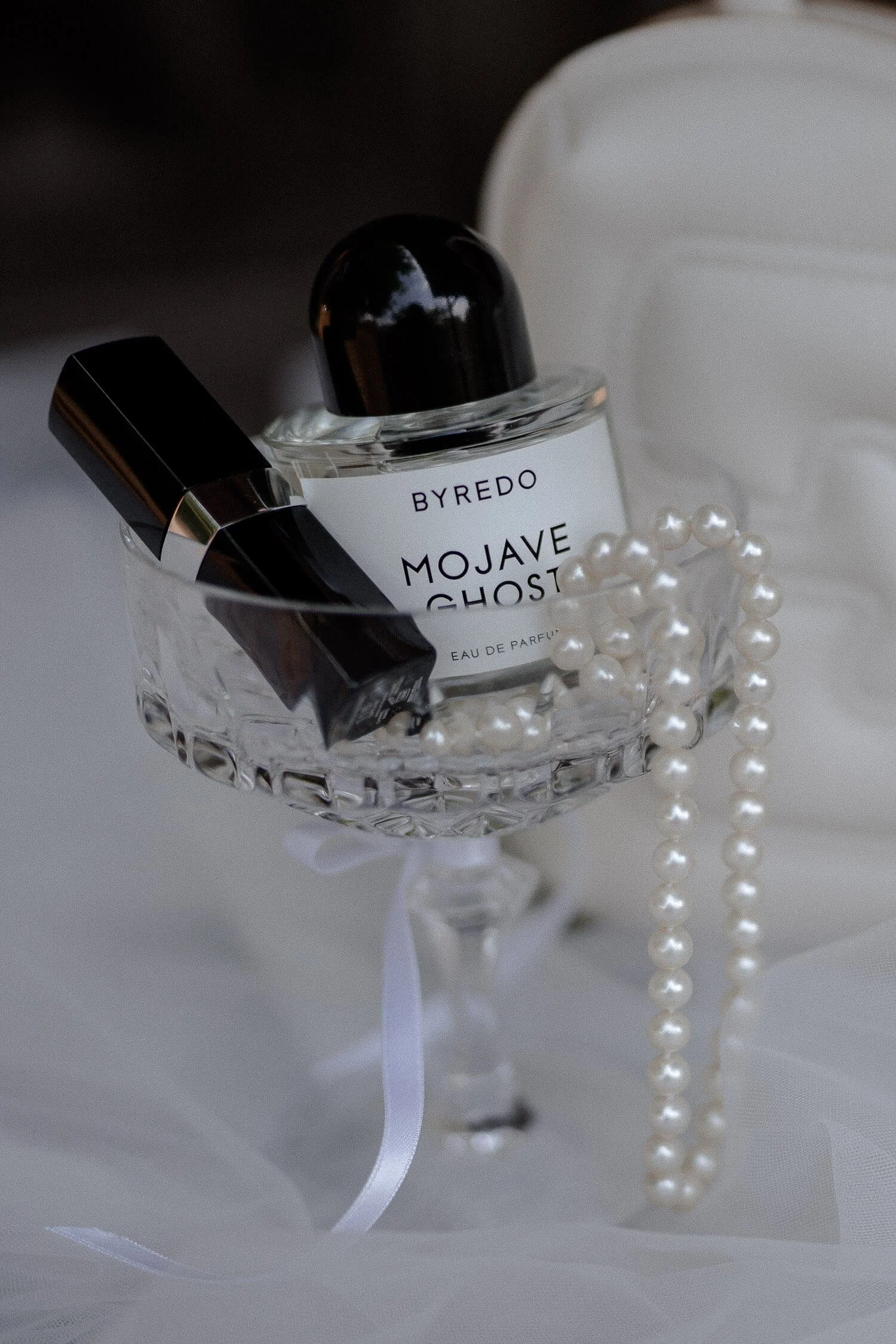 Hochzeitsdetails mit Parfum, Lippenstift und Perlen im Glas.