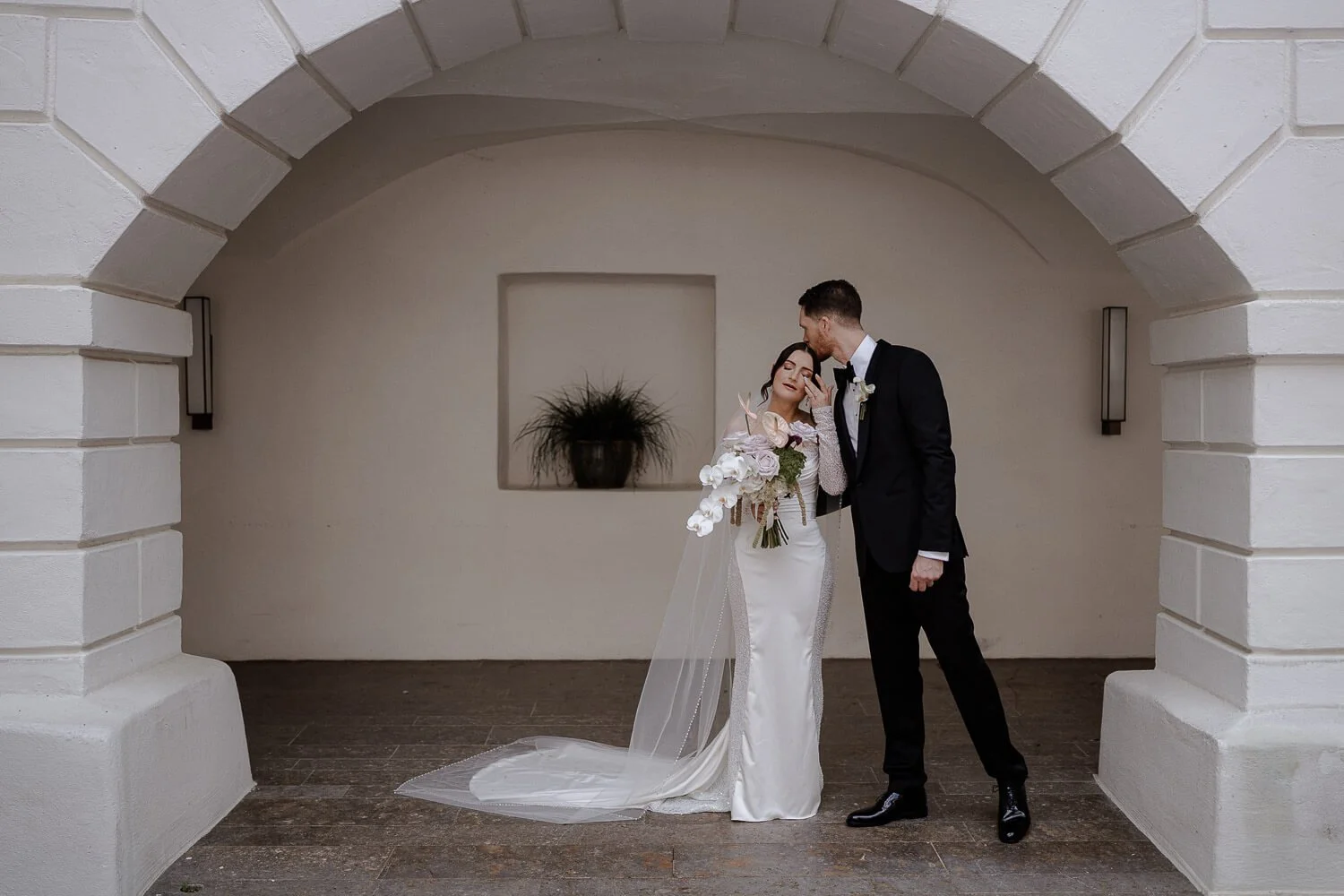 Brautpaar küsst sich unter historischem Torbogen.