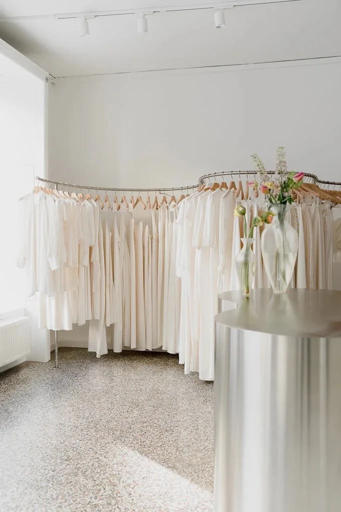 Brautmode München: helle Boutique mit minimalistischer Kleiderstange und Blumen