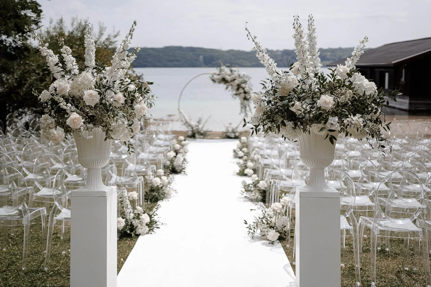 Blumendeko Hochzeit am See: weiße Rosen in Vasen am Gang zur Trauung