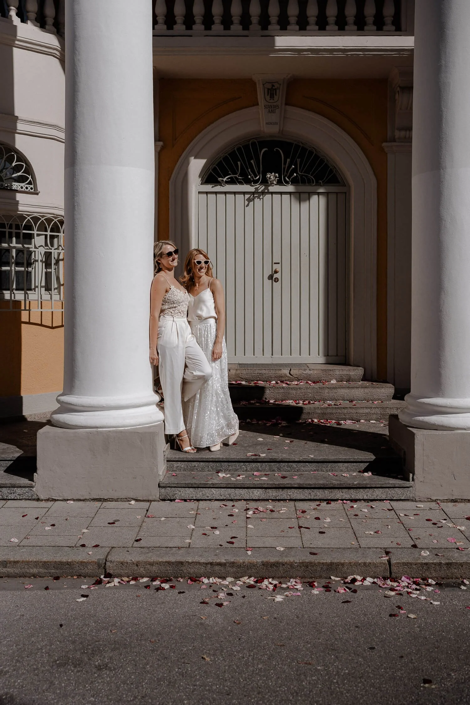 Hochzeitspaar vor dem Standesamt Mandelstrasse in München, umgeben von Säulen und Rosenblättern.