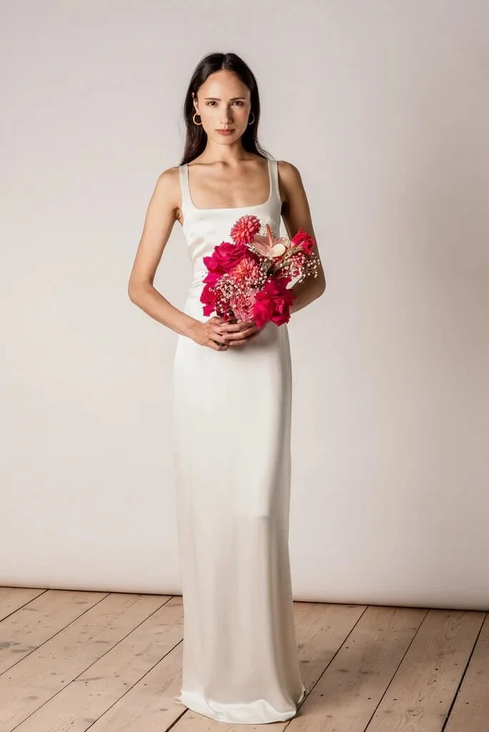 Brautmode in München: Model im schlichten Brautkleid mit pinkem Brautstrauß