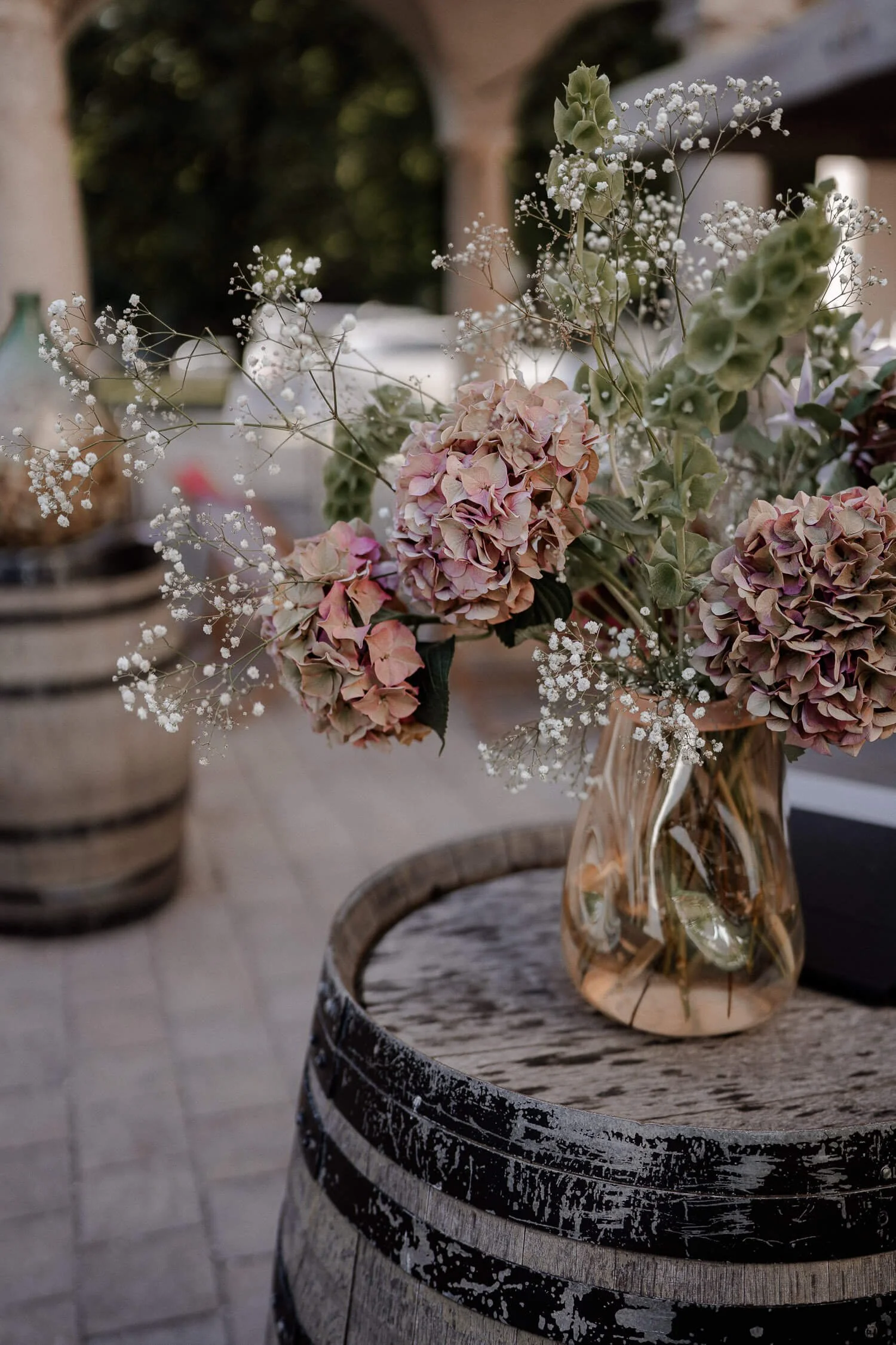 Vase mit Hochzeitsblumen auf rustikalem Fass in Münchner Hochzeitslocation