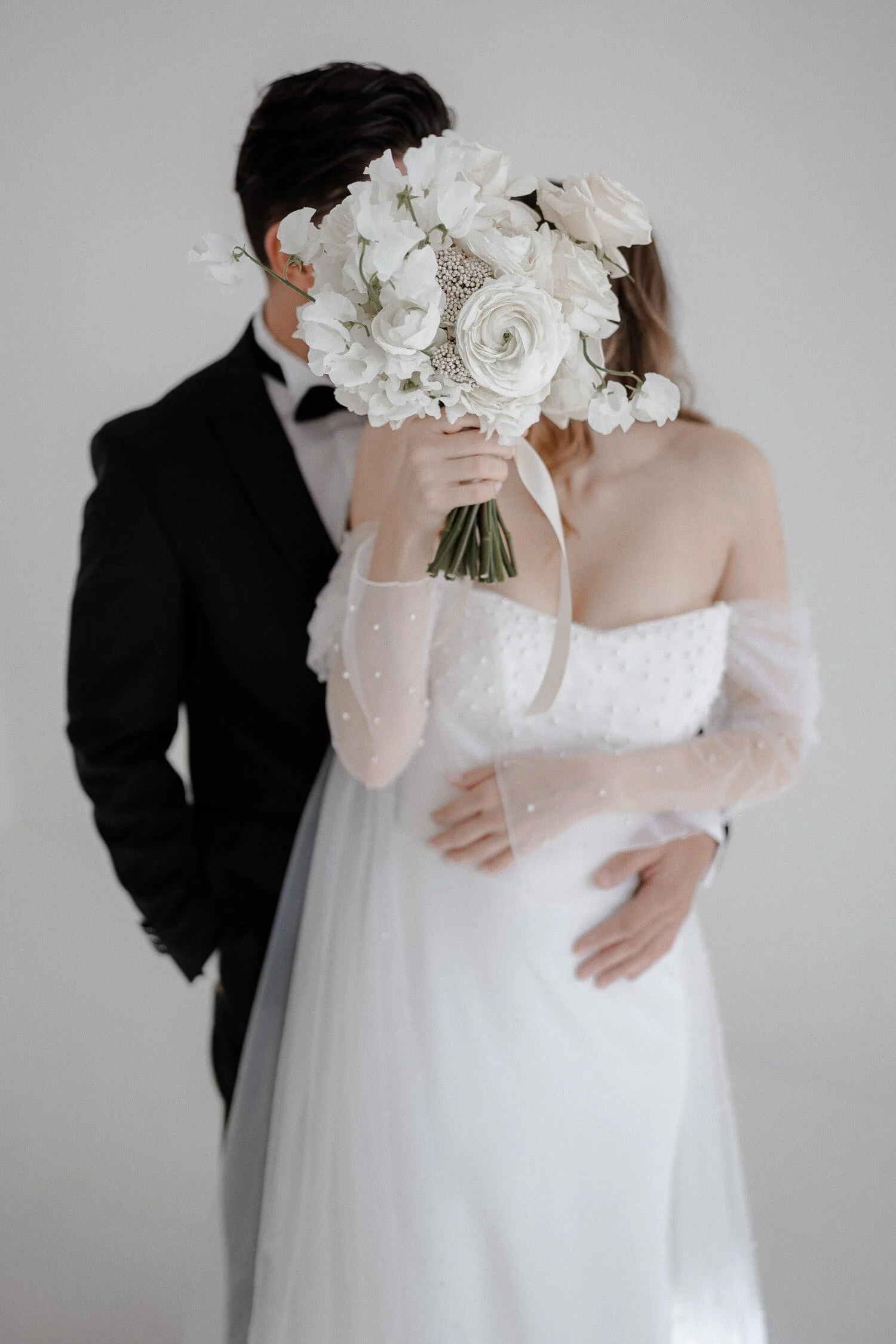 Hochzeit Blumendeko: Brautpaar mit weißem Strauß als Portrait vor neutralem Hintergrund