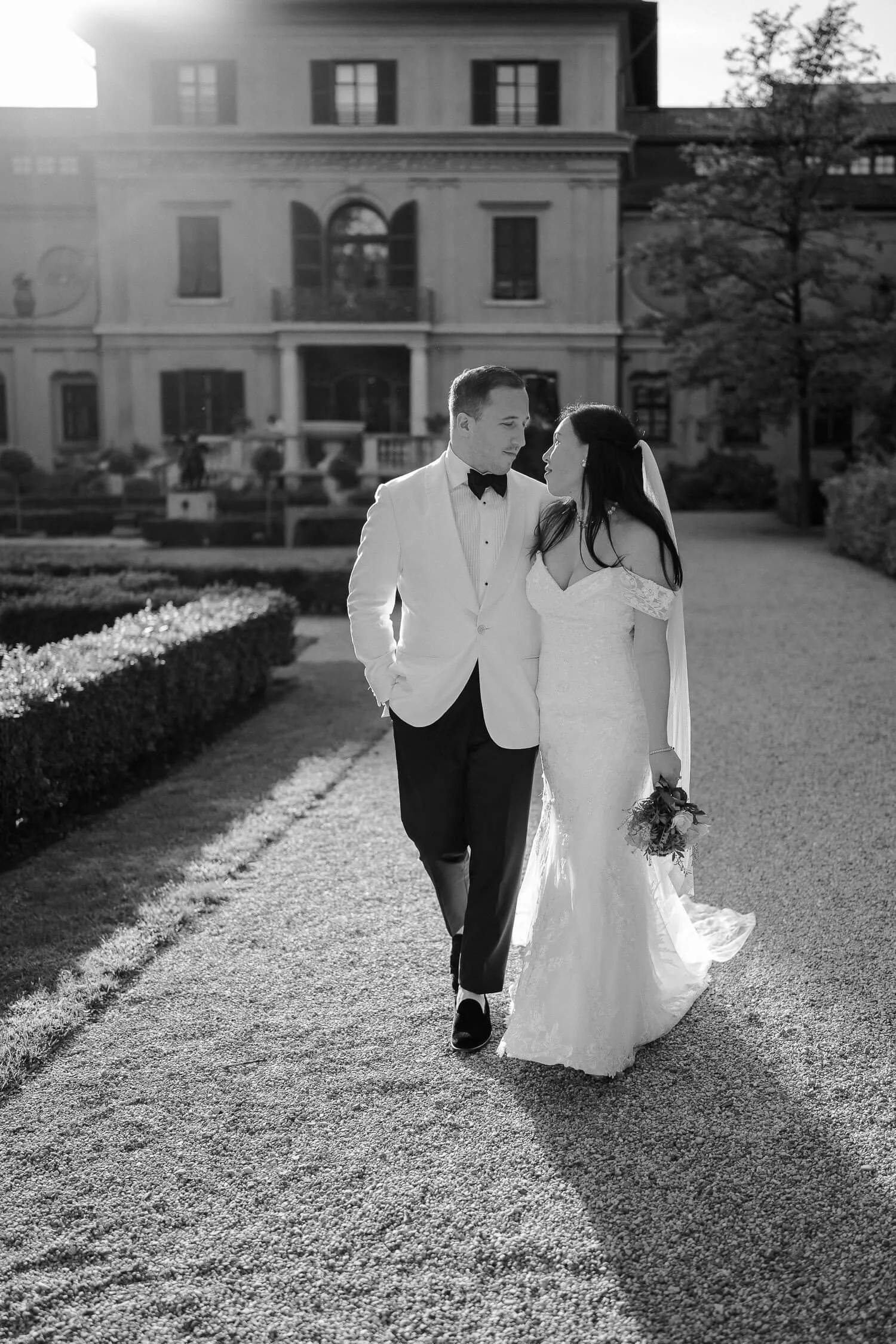 Romantisches Hochzeitsfoto in München – Braut und Bräutigam spazieren verliebt vor eleganter Villa mit italienischem Flair