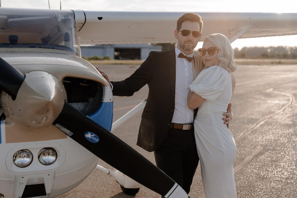 Couple posing next to small airplane at golden hour