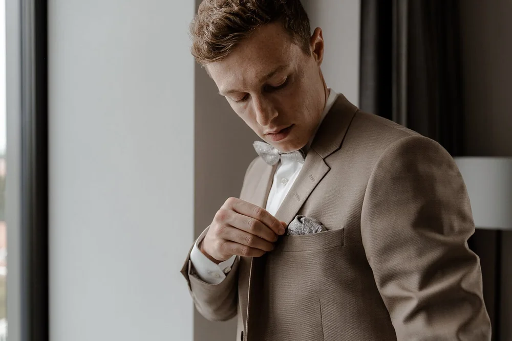 Groom adjusting pocket square by window light