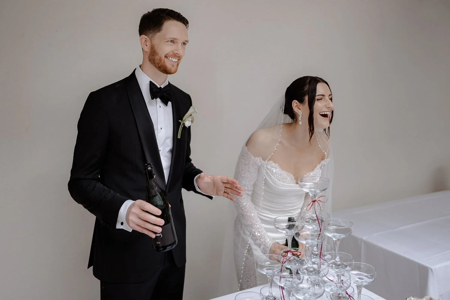 Hochzeitspaar lacht beim Sektempfang mit Champagnerturm.