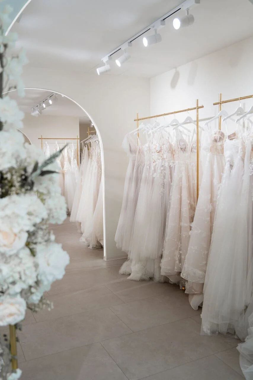 brautmode münchen: Kleiderwand mit Spitzengowns an goldenen Stangen im Atelier