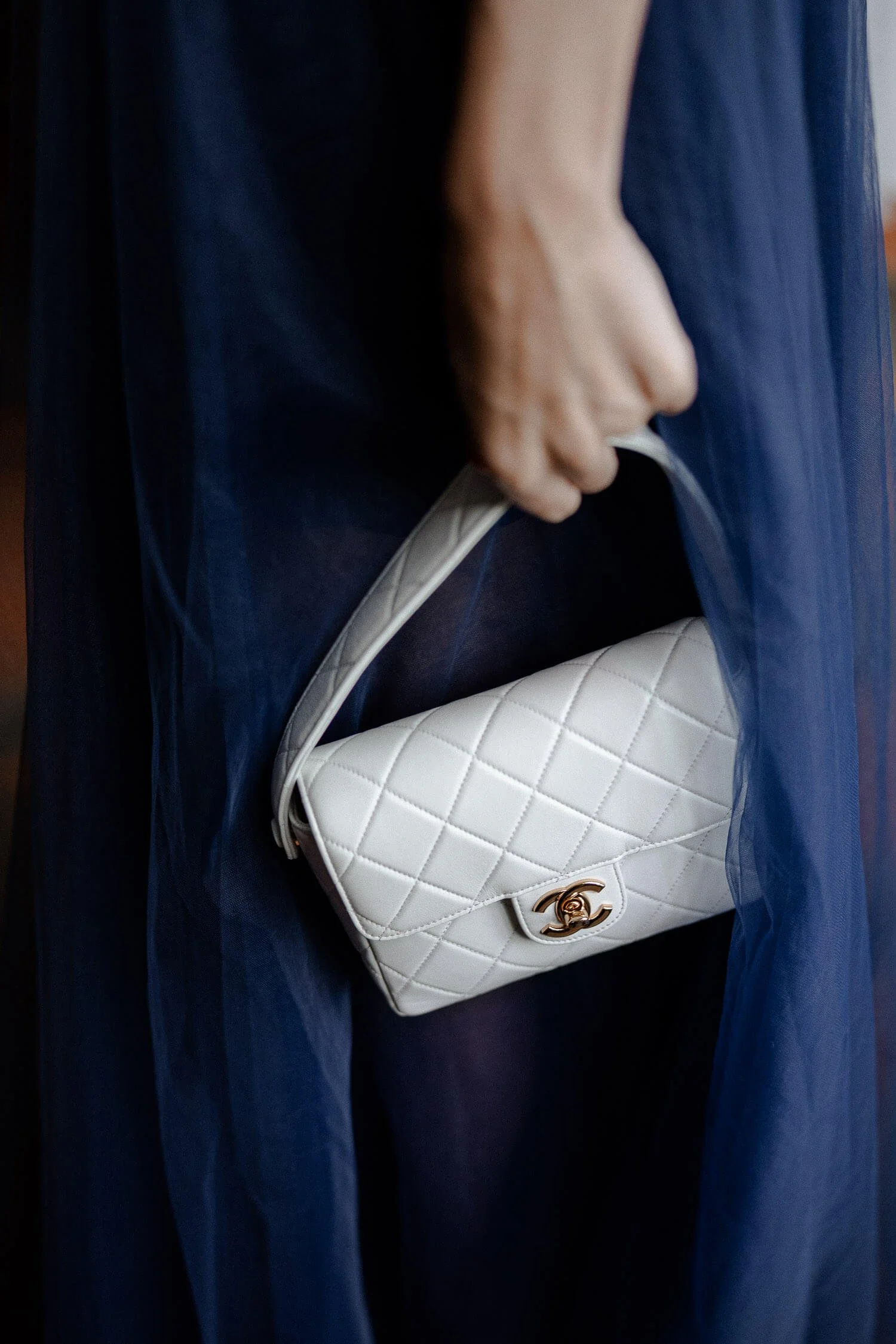 Weiße Chanel Handtasche von einem Hochzeitsgast vor blauen Kleid.