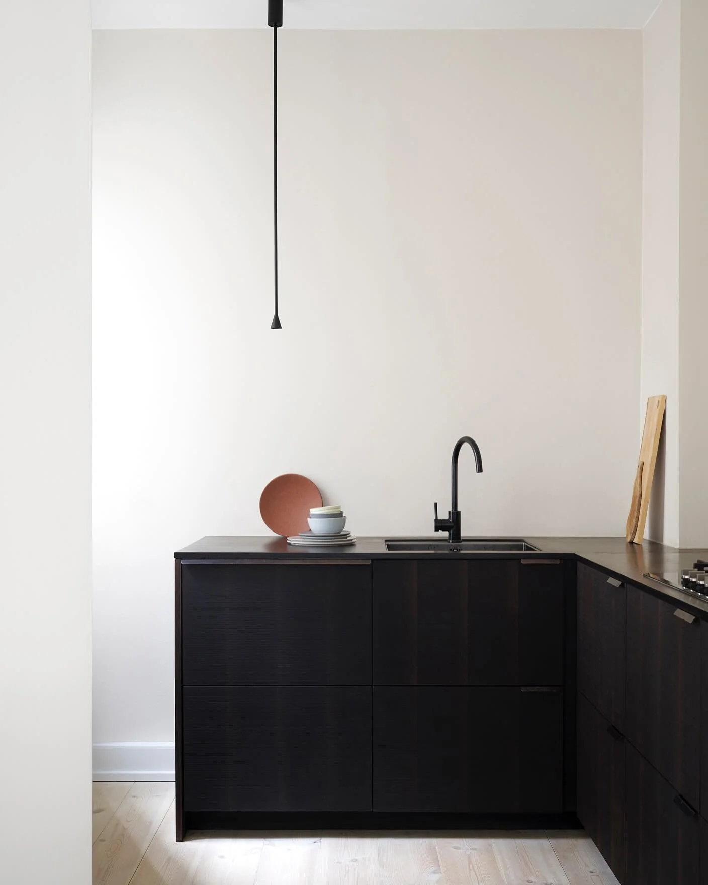 SIMPLE ELEGANCE - This kitchen stands out with its dark wood fronts, creating a striking contrast within the space. This design embodies a graphic aesthetic, enhanced by the sleek hanging lamps suspended from the ceiling. 

The overall expression is 