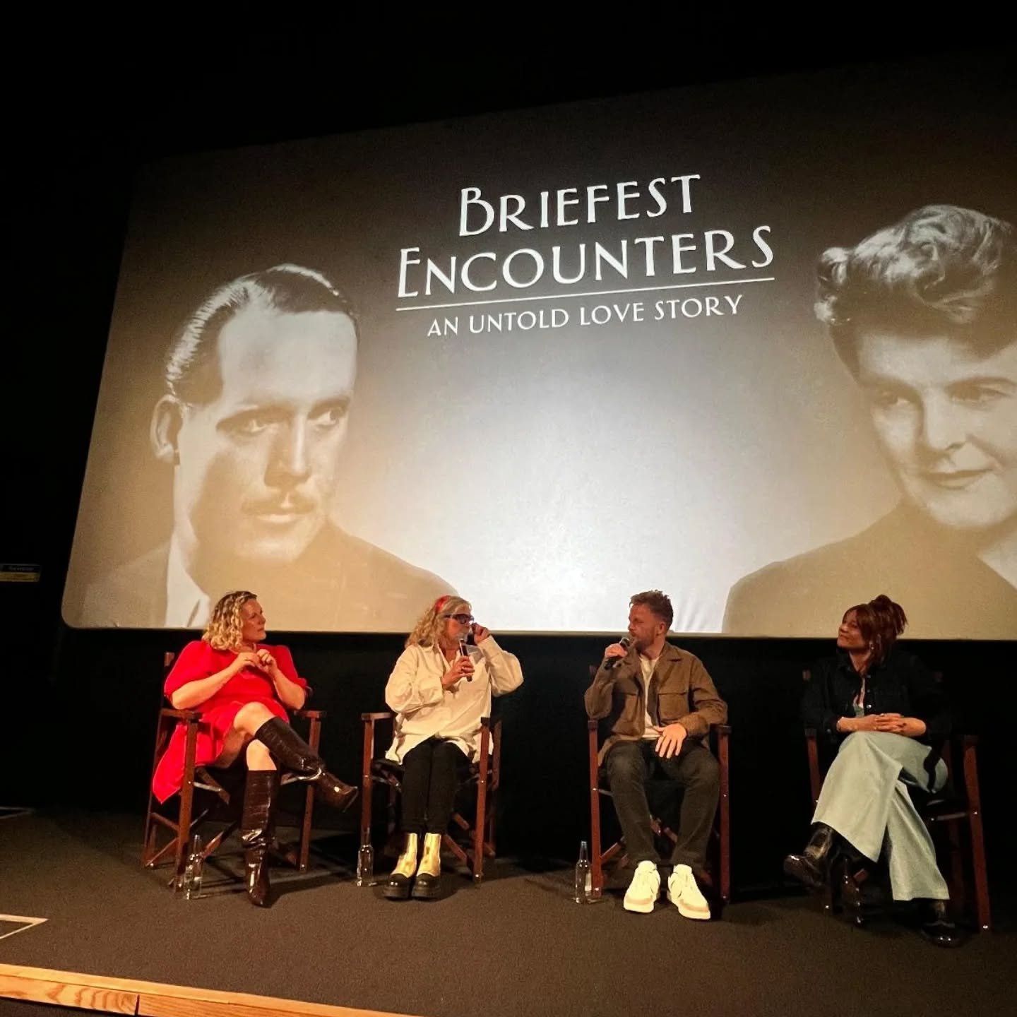 Four people seated on a stage, engaged in a panel discussion, with a large screen behind them displaying a black-and-white photo of a man and woman and the text 'Briefest Encounters: An Untold Love Story'.